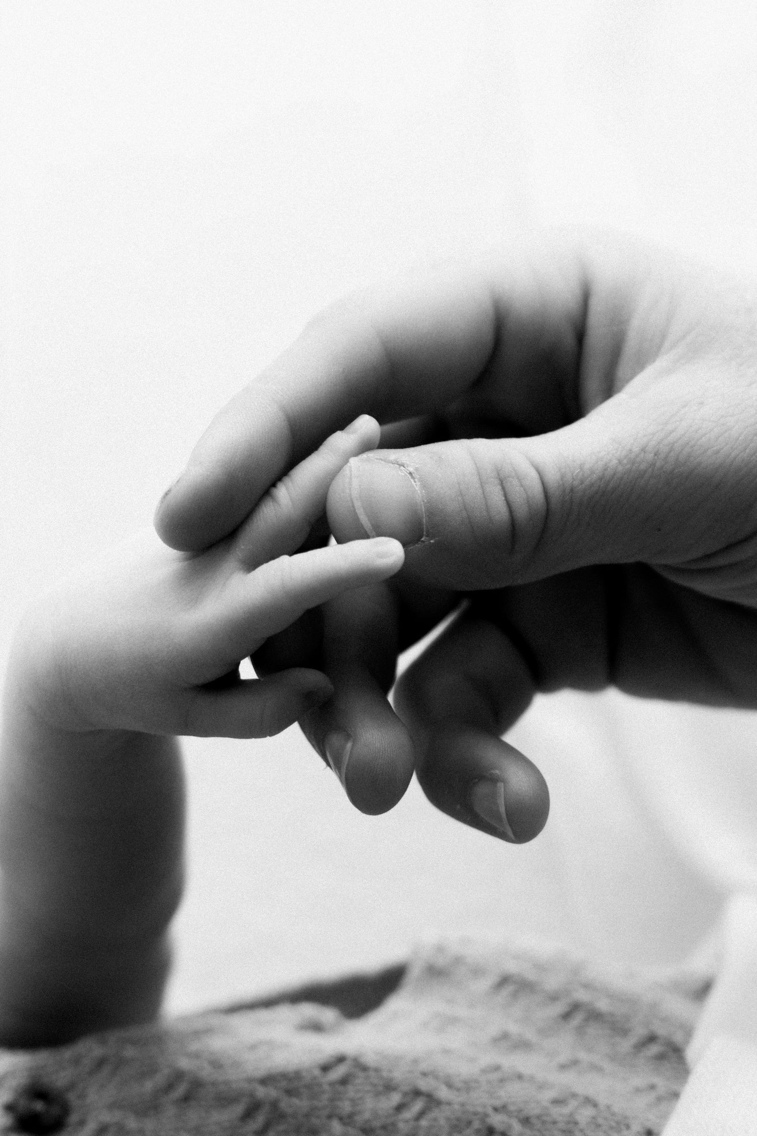 Black and white close-up image of hands reaching out to touch each other across a textured surface.