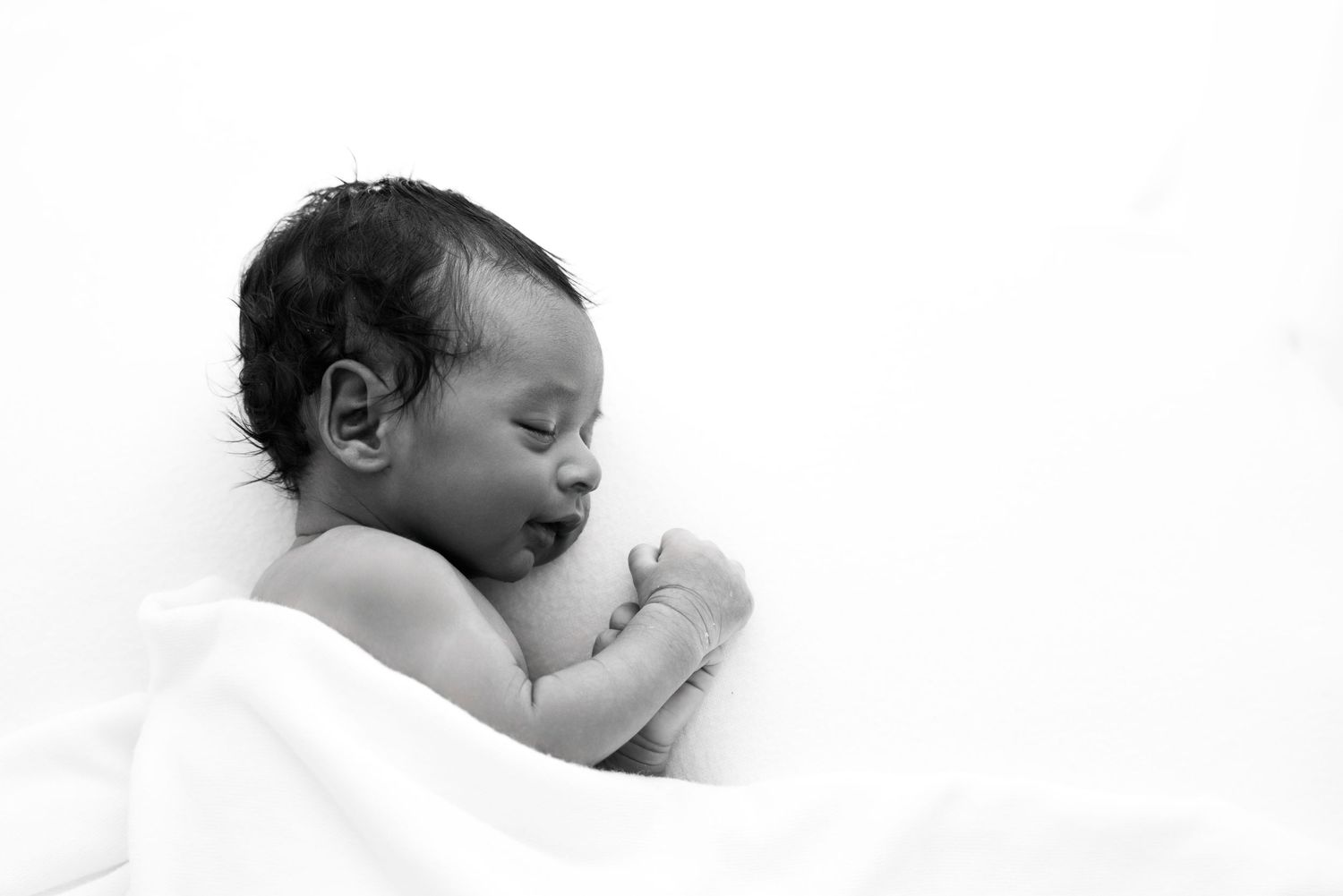Peaceful black and white portrait of a sleeping newborn against soft white fabric.