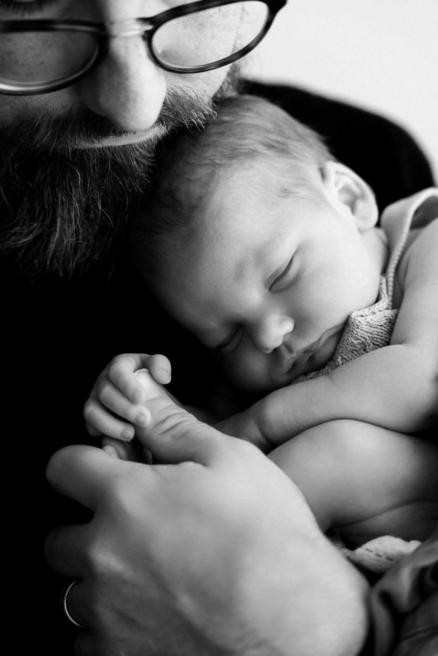A sleeping baby rests peacefully in black and white while holding onto someone's hand.