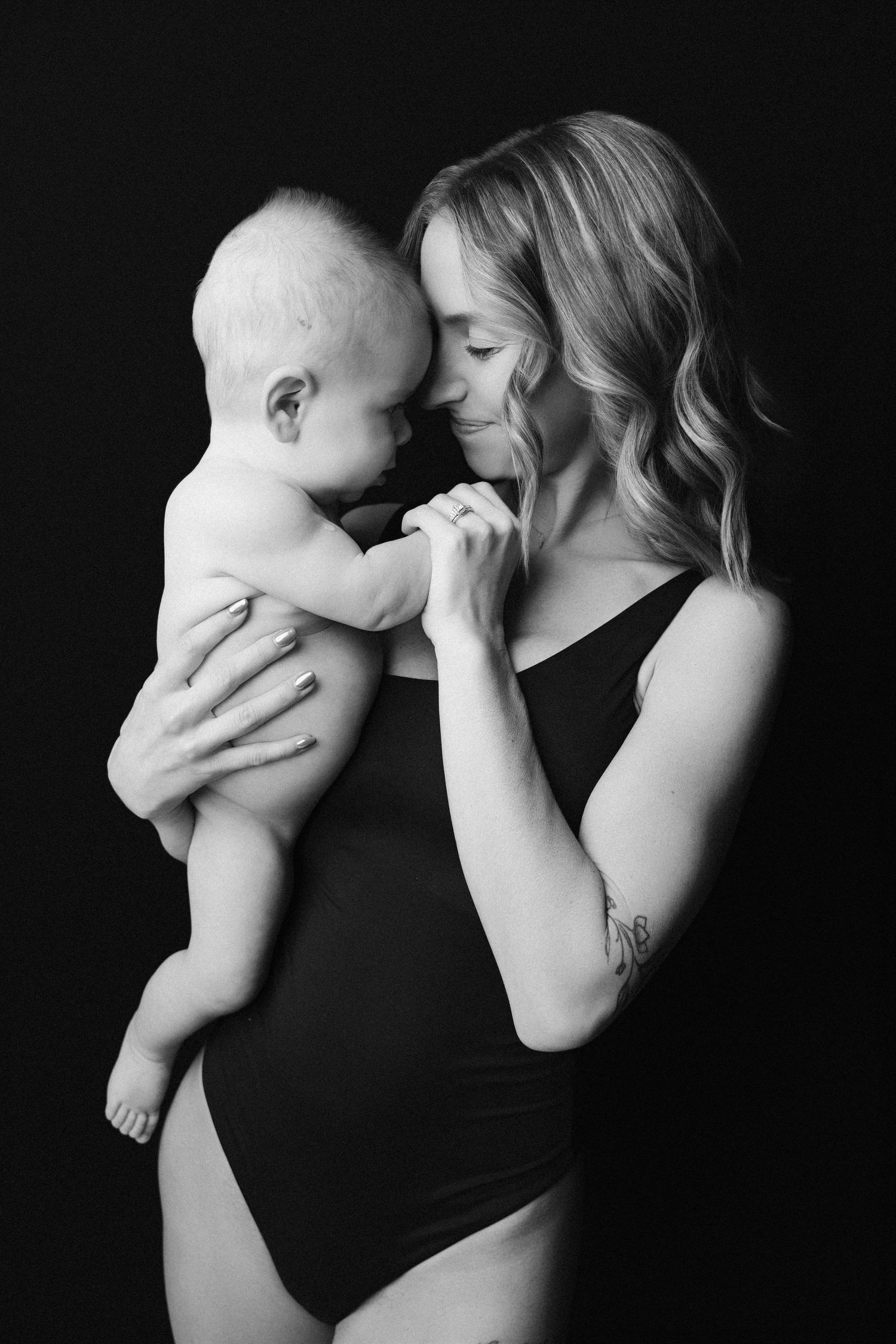 Black and white artistic photo series showing tender moments between a parent and infant against dark background.