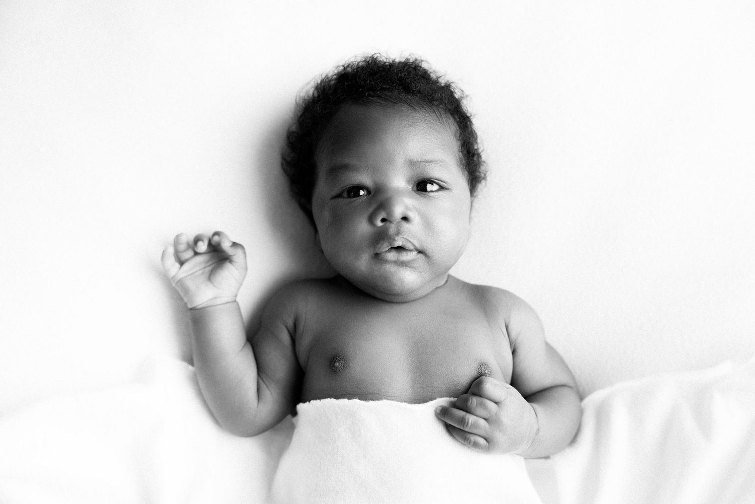 Three adorable babies lying on white sheets in black and white photography.
