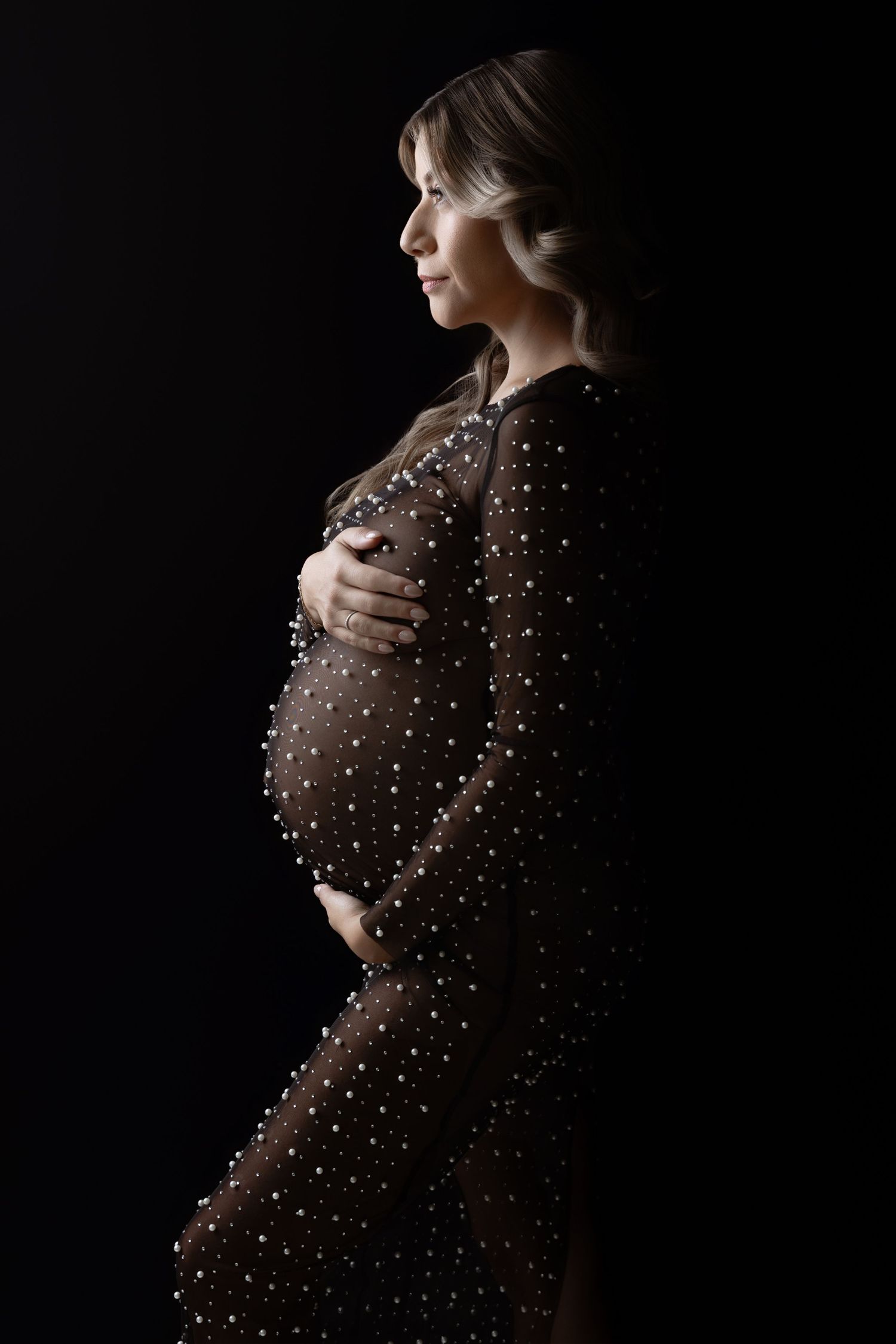 Elegant maternity portrait in dark brown polka dot dress against black background showing side profile silhouette.