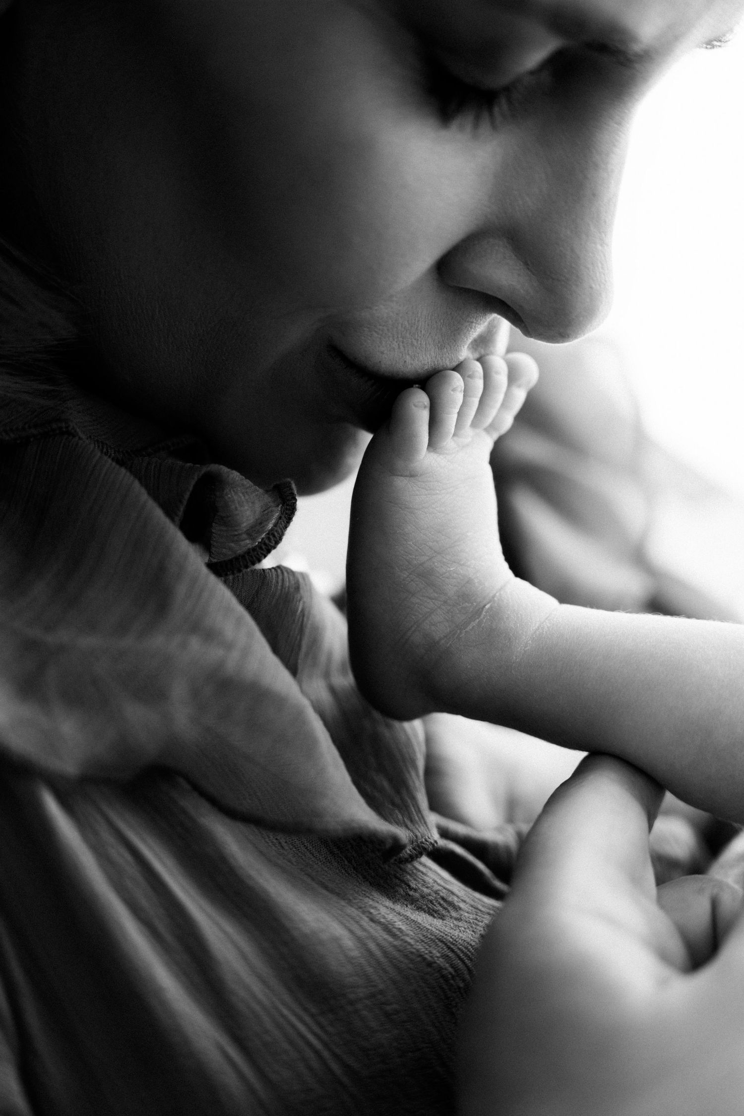 A tender black and white portrait showing a parent gently kissing their baby's tiny foot.