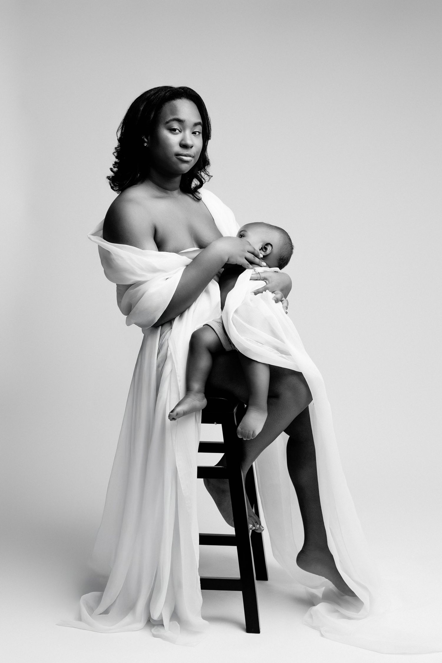 Black and white artistic studio portraits of figure in flowing white dress seated on dark stool in minimalist setting.