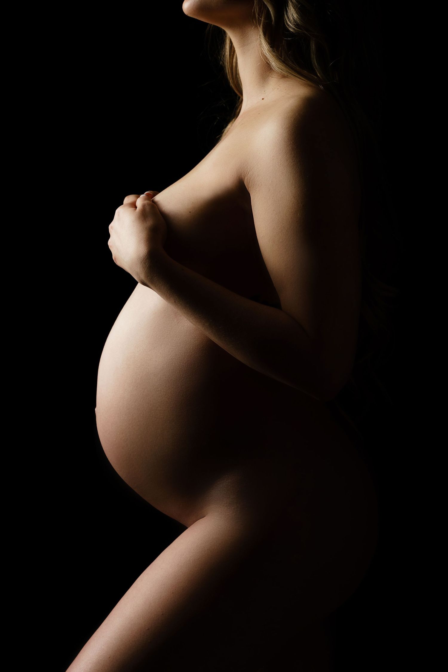 Artistic side-profile silhouettes highlighting pregnancy curves against dark background.