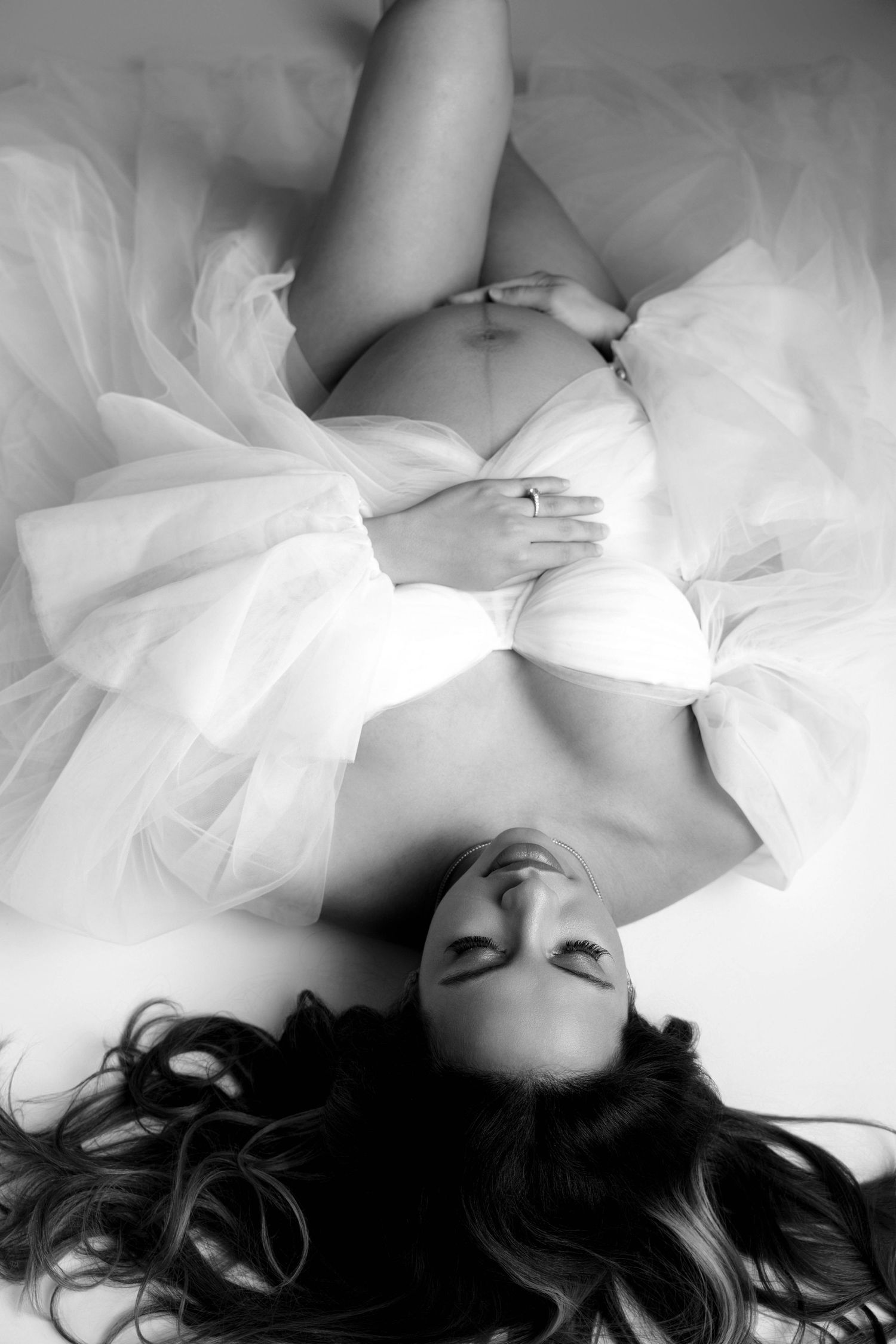 Ethereal overhead maternity portrait with subject lying on white tulle fabric.