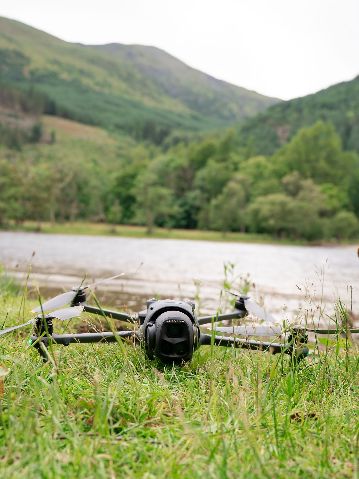 Drone camera equipment lying in green grass with mountains and lake in background.