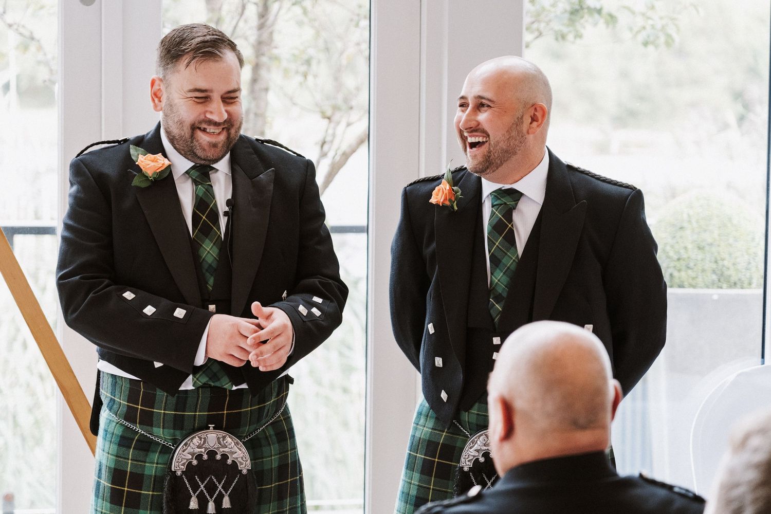 Wedding party members in traditional Scottish kilts share laughter and drinks during a celebration.