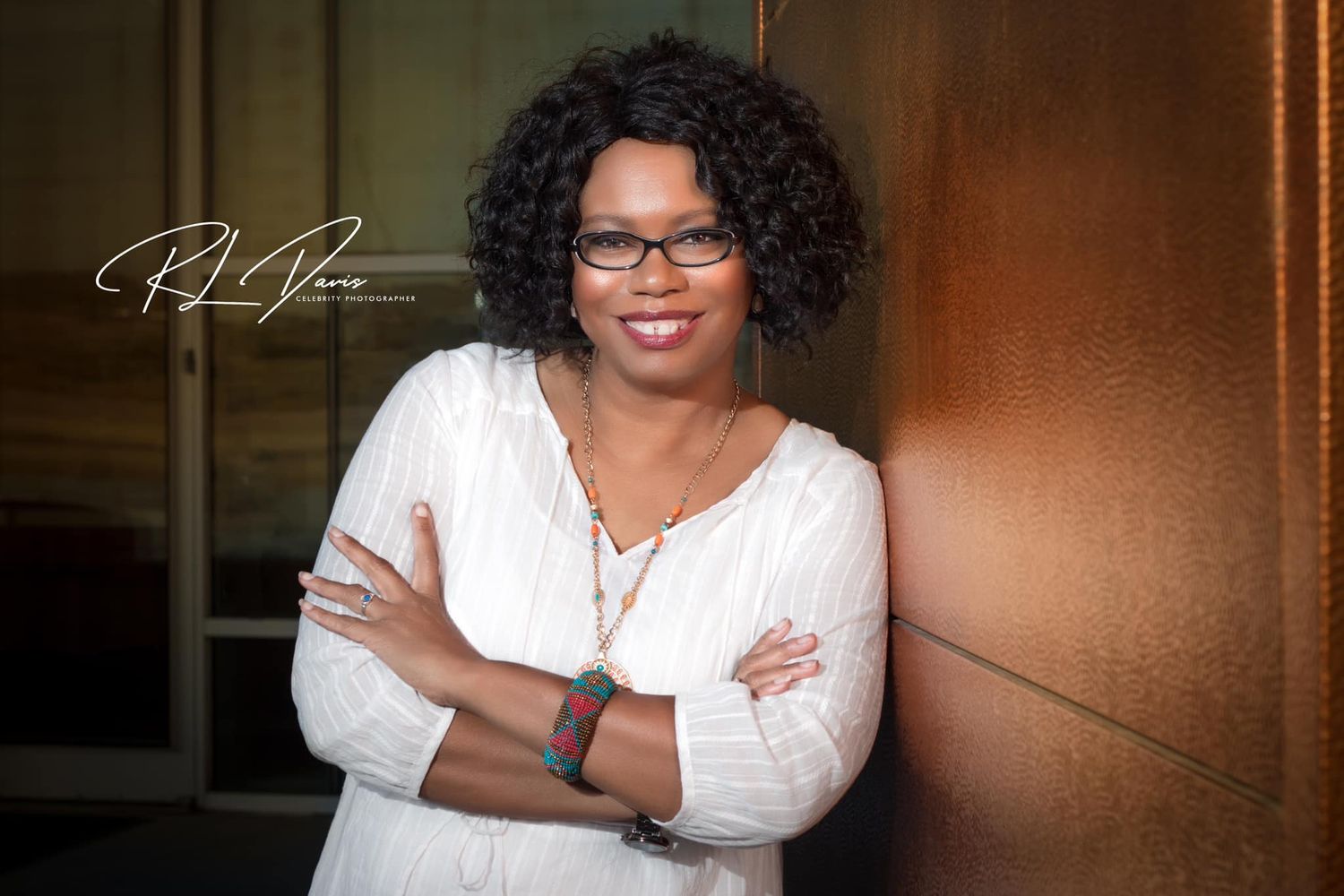 Professional portrait of woman in white top smiling warmly against warm-toned background. Photographer RL Davis