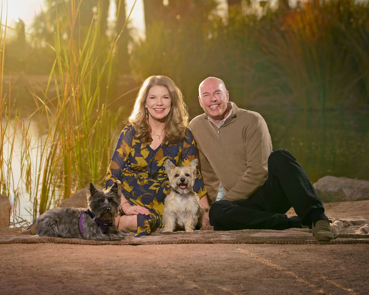 A couple relaxes on the ground with their small dogs during golden hour. Photographer RL Davis