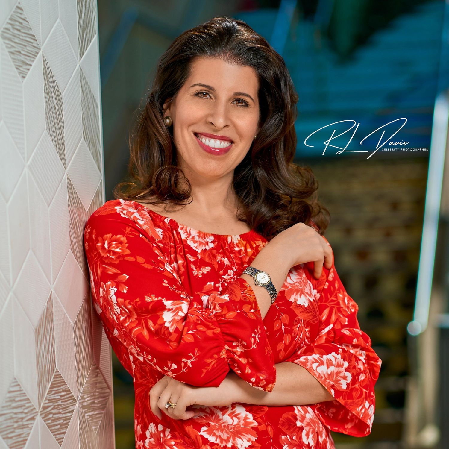 Professional portrait of woman in red floral dress leaning against patterned wall. Photographer RL Davis