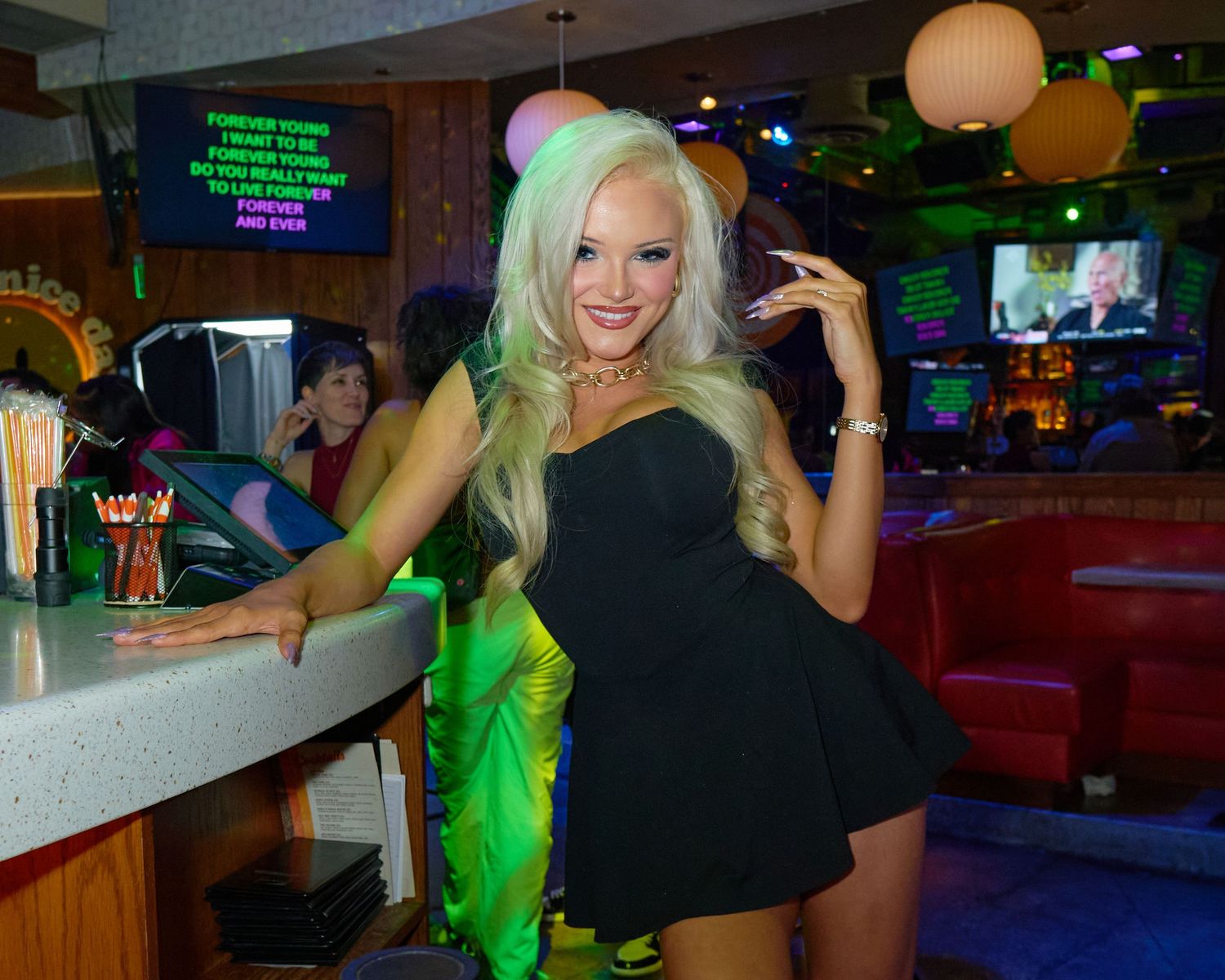 Group of people dancing and socializing in a bar with neon green lighting and paper lantern decorations.