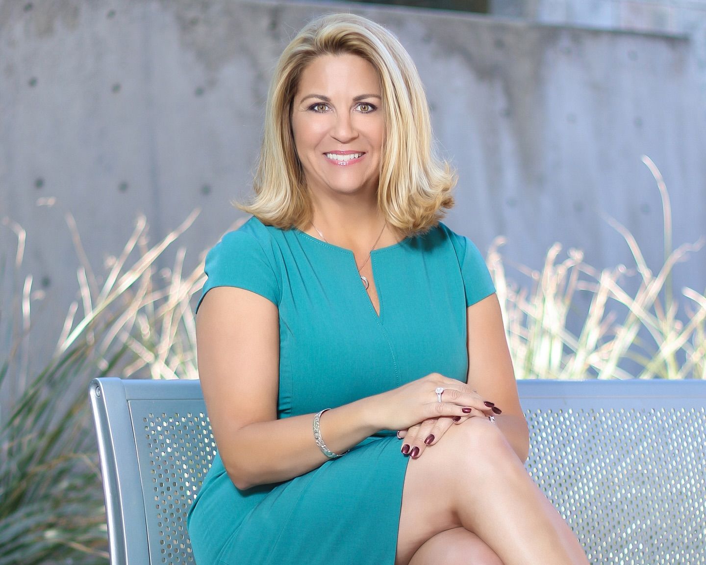 Professional portrait of woman in teal dress seated outdoors on modern patio furniture. Photographer RL Davis