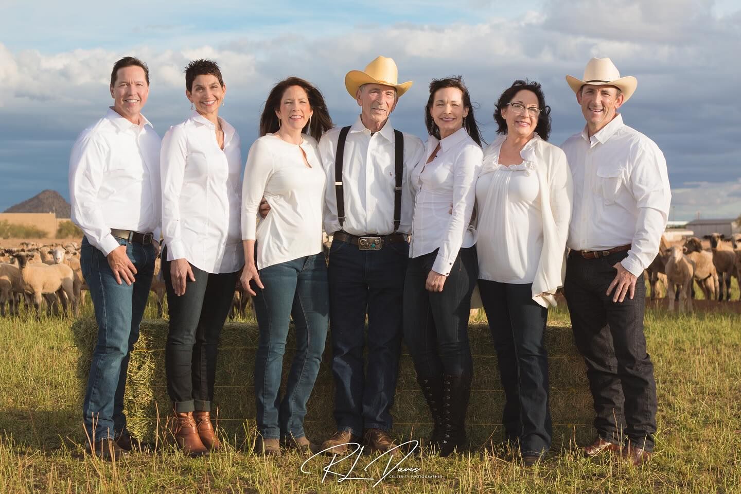 A group of people in white shirts and jeans pose together outdoors against a cloudy sky. Photographer RL Davis