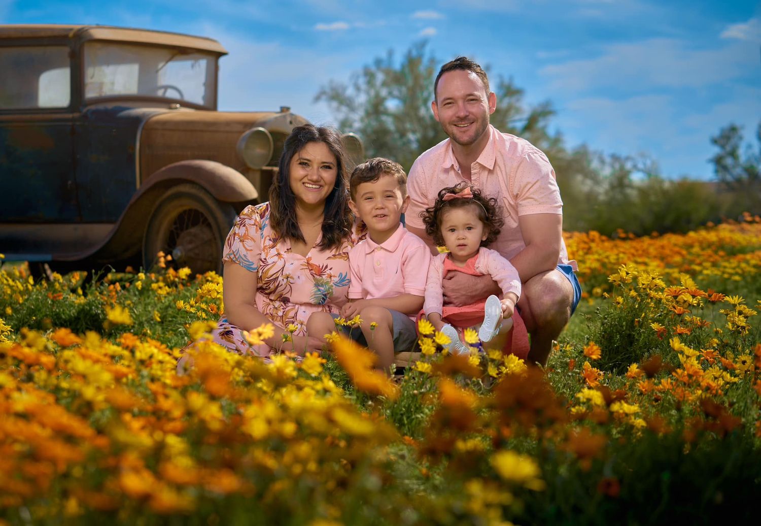 Family lying together in vibrant field of orange wildflowers on sunny day. Photographer RL Davis