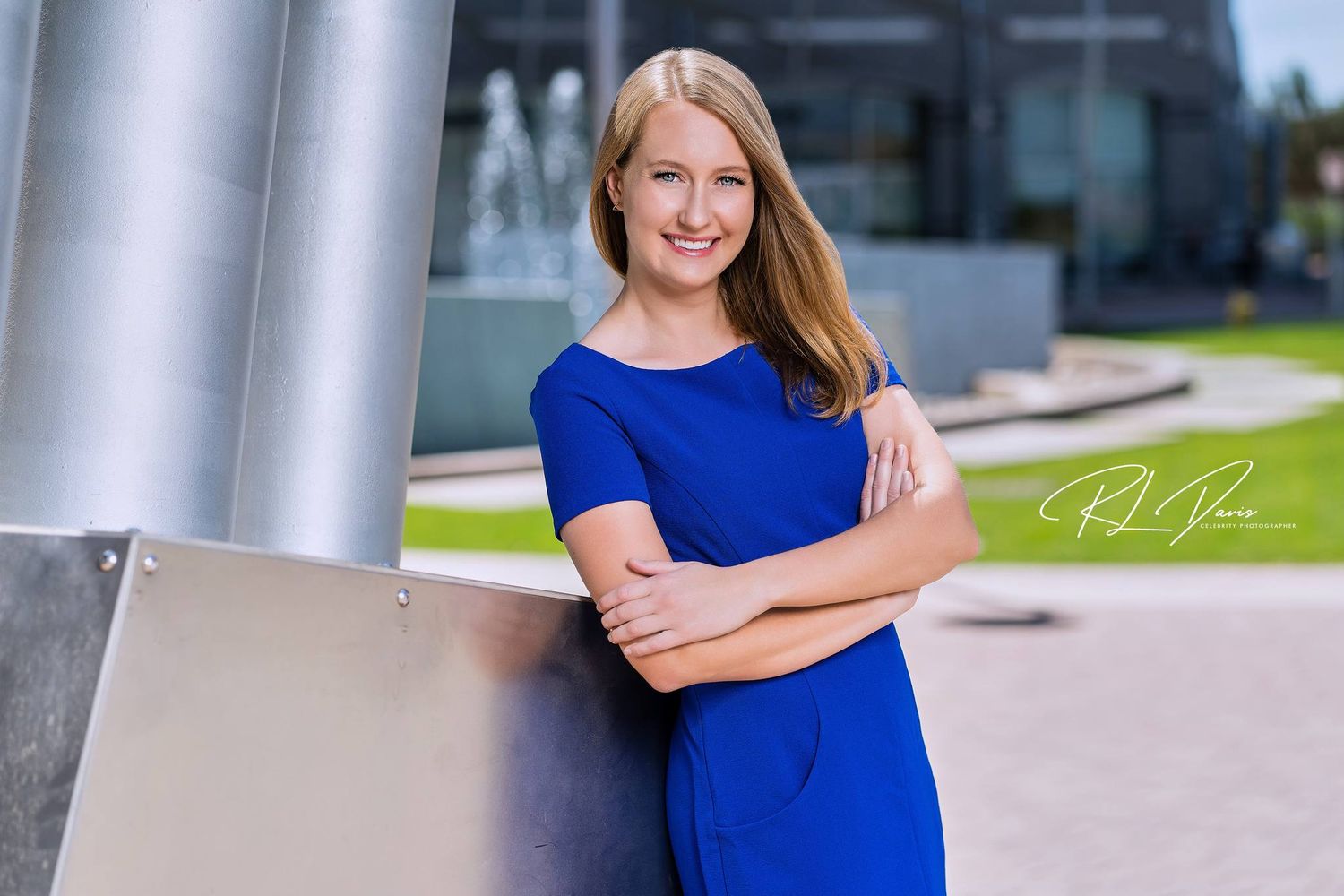 Professional headshot of woman in blue dress standing by modern architectural columns. Photographer RL Davis