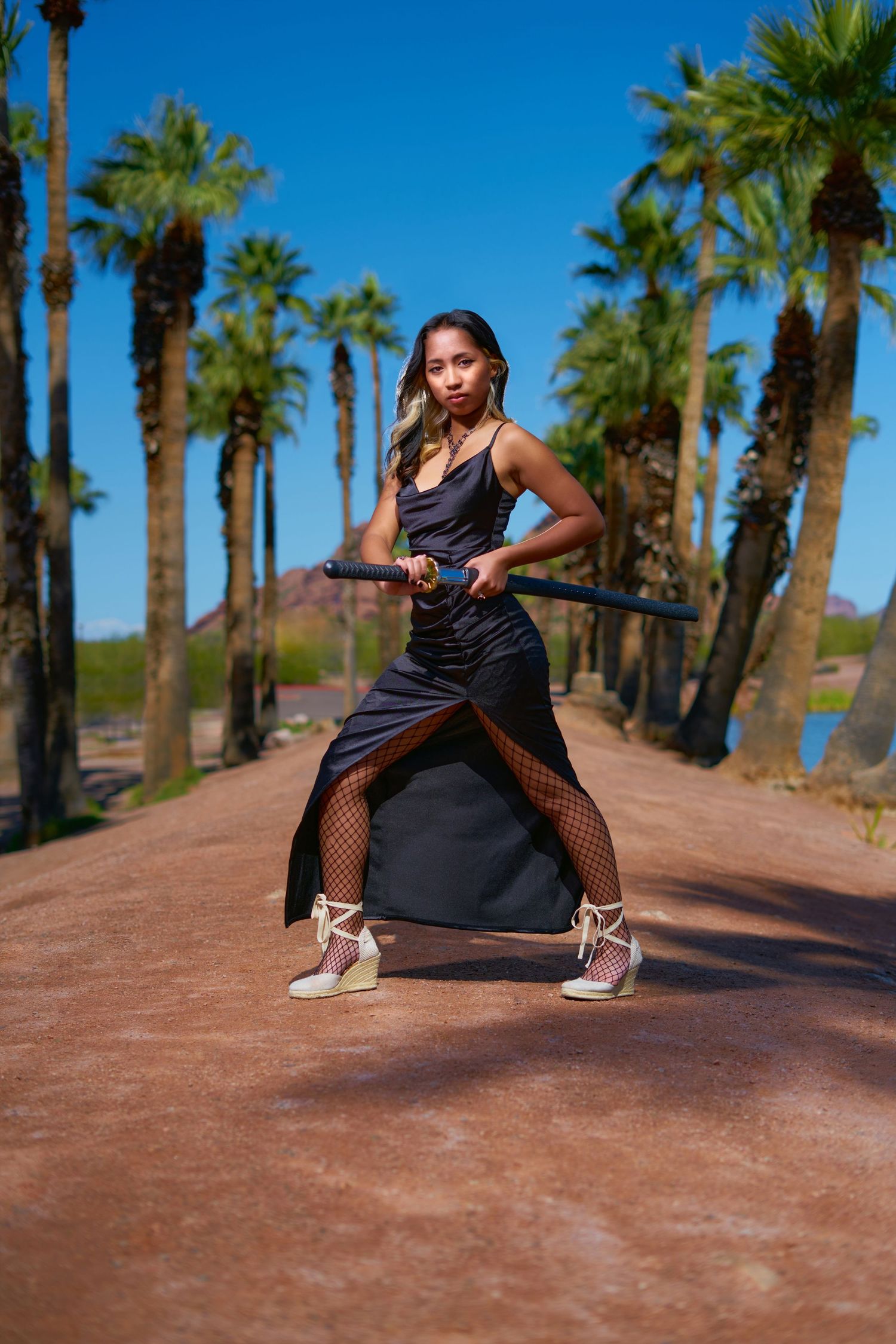 Athletic dancer in black outfit strikes dynamic pose on palm tree-lined path under bright blue sky. Photographer RL Davis