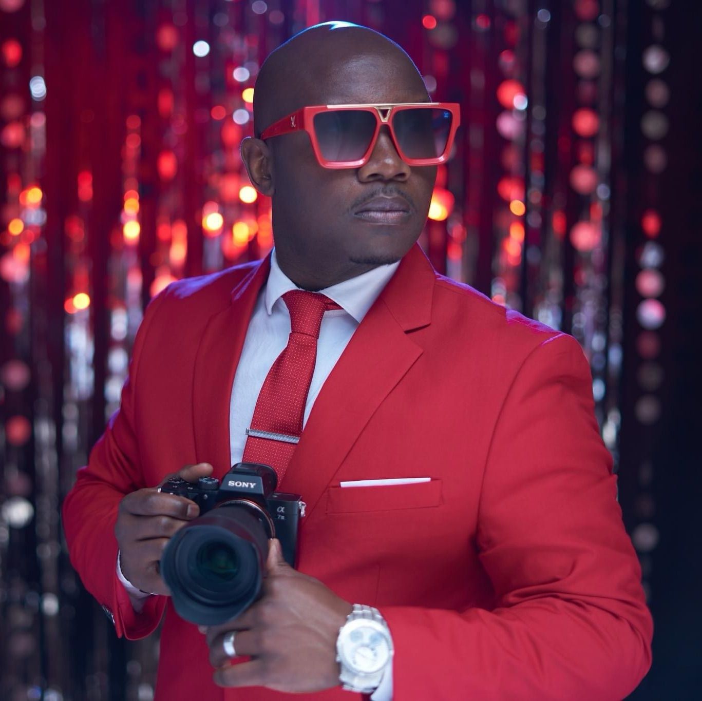 Photographer in striking red suit poses with camera equipment against sparkly backdrop. Photographer RL Davis