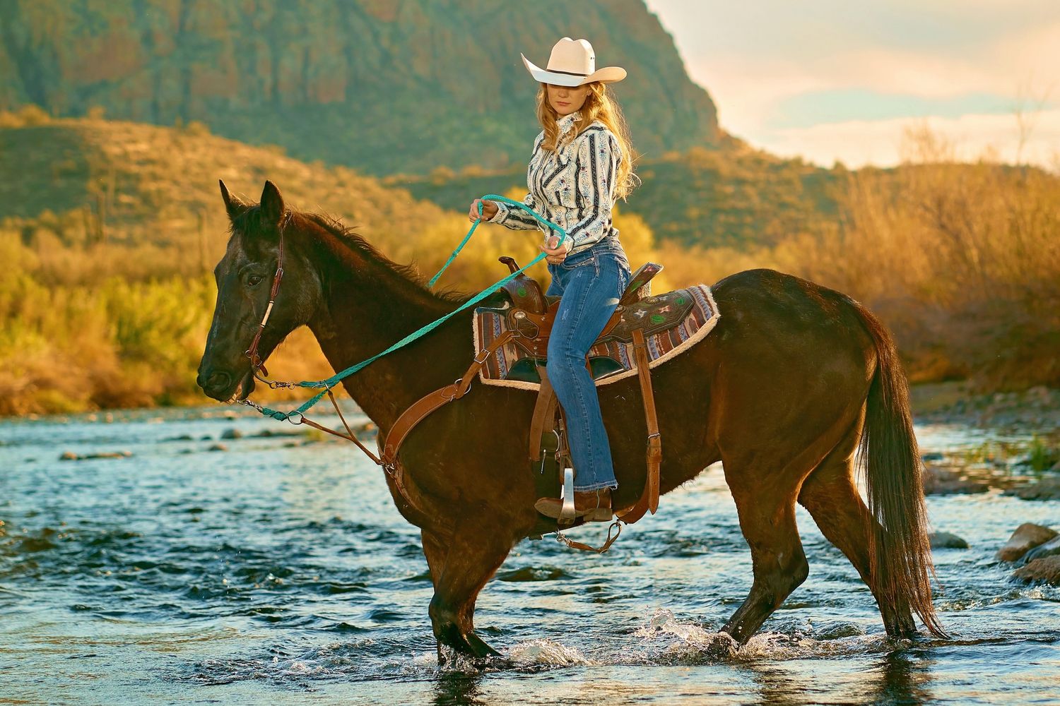 Horses wading through the salt river water during golden sunset with mountain backdrop. Photographer RL Davis