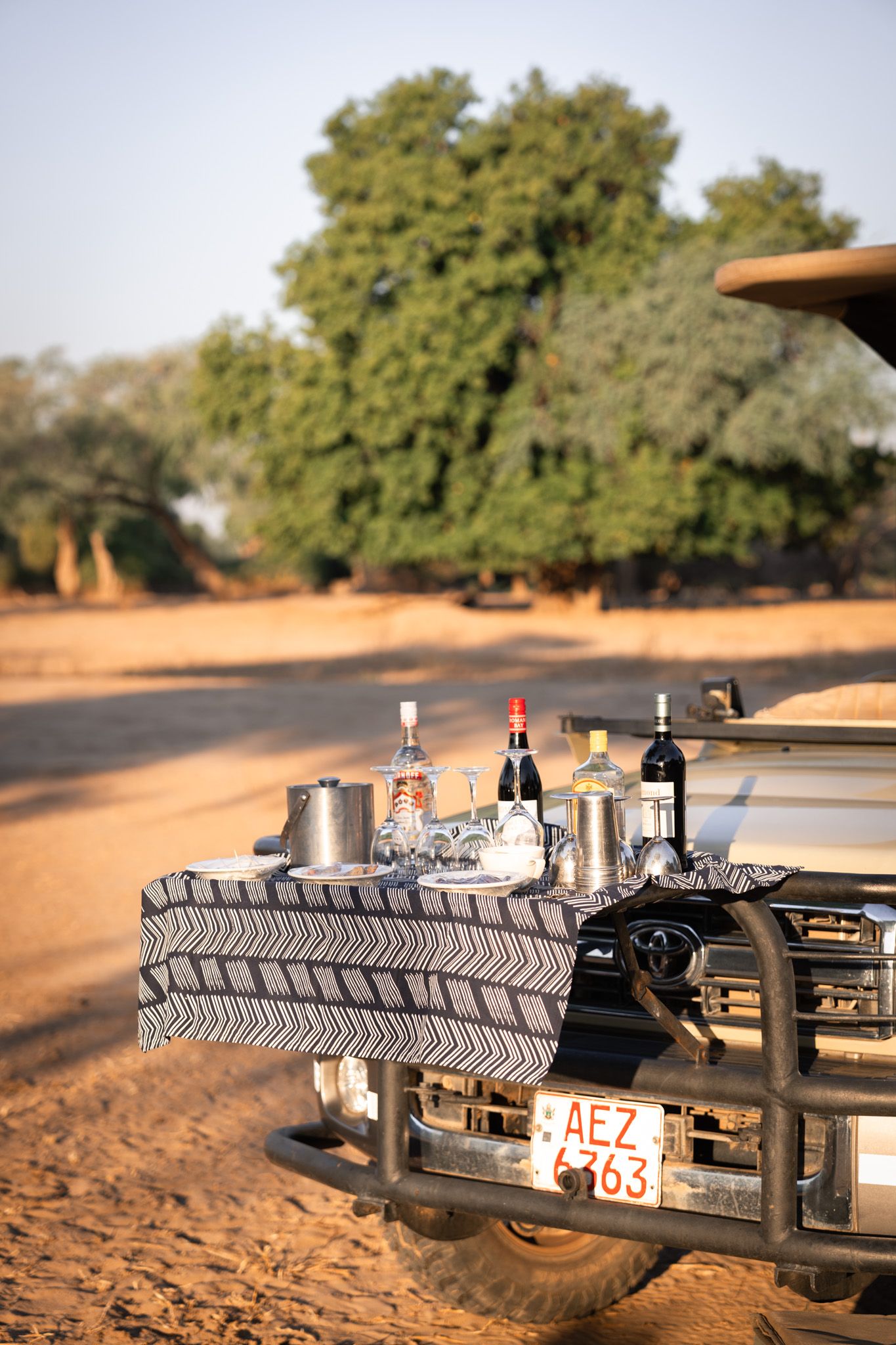 Liquor bottles displayed on a spare tire rack of an off-road vehicle in a dusty outdoor setting.