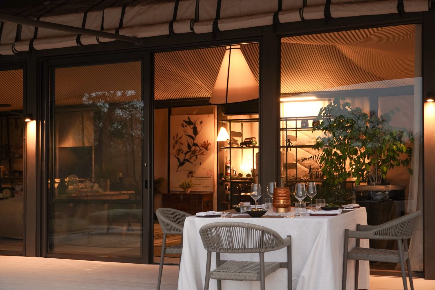 Elegant dining setup with white tablecloth and ambient lighting in glass-enclosed restaurant.