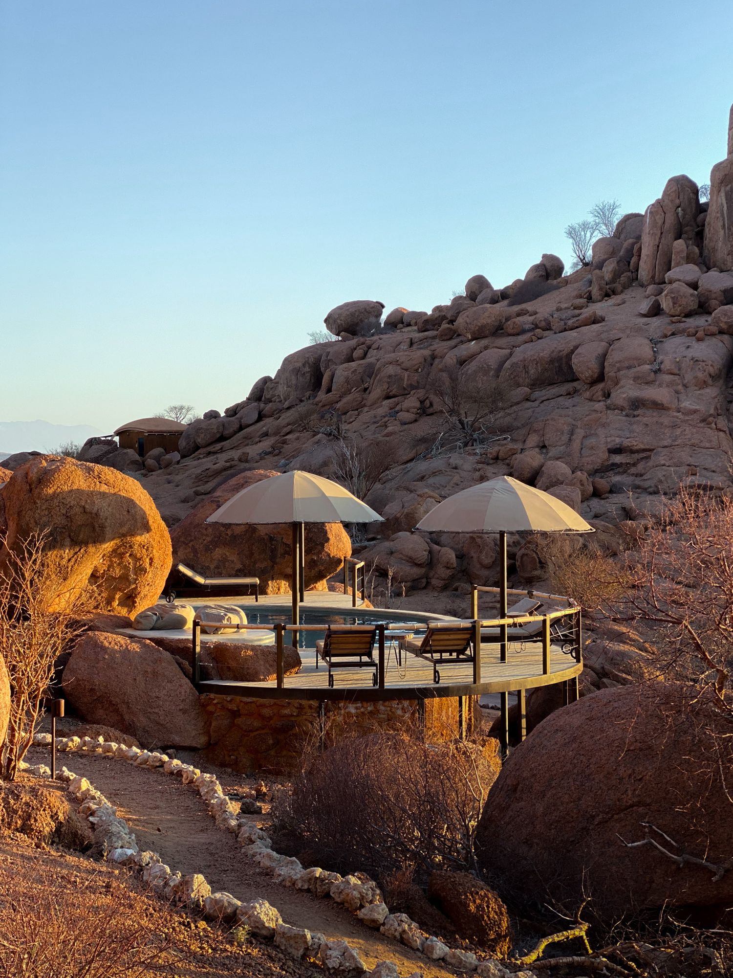 Desert rock formation with circular viewing deck featuring white umbrellas and lounge furniture.