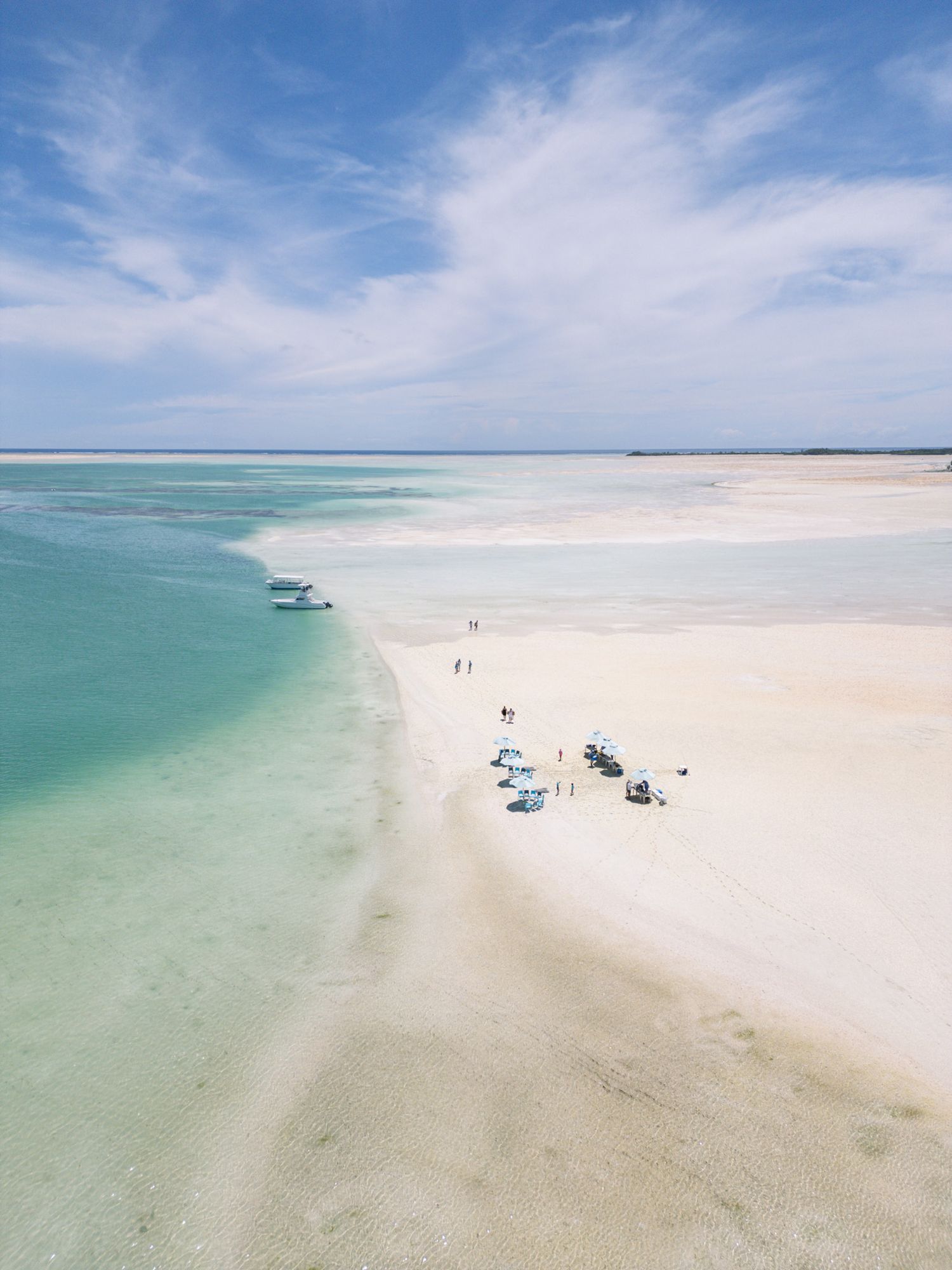Aerial view of boats parked on a pristine white sand beach alongside turquoise waters.