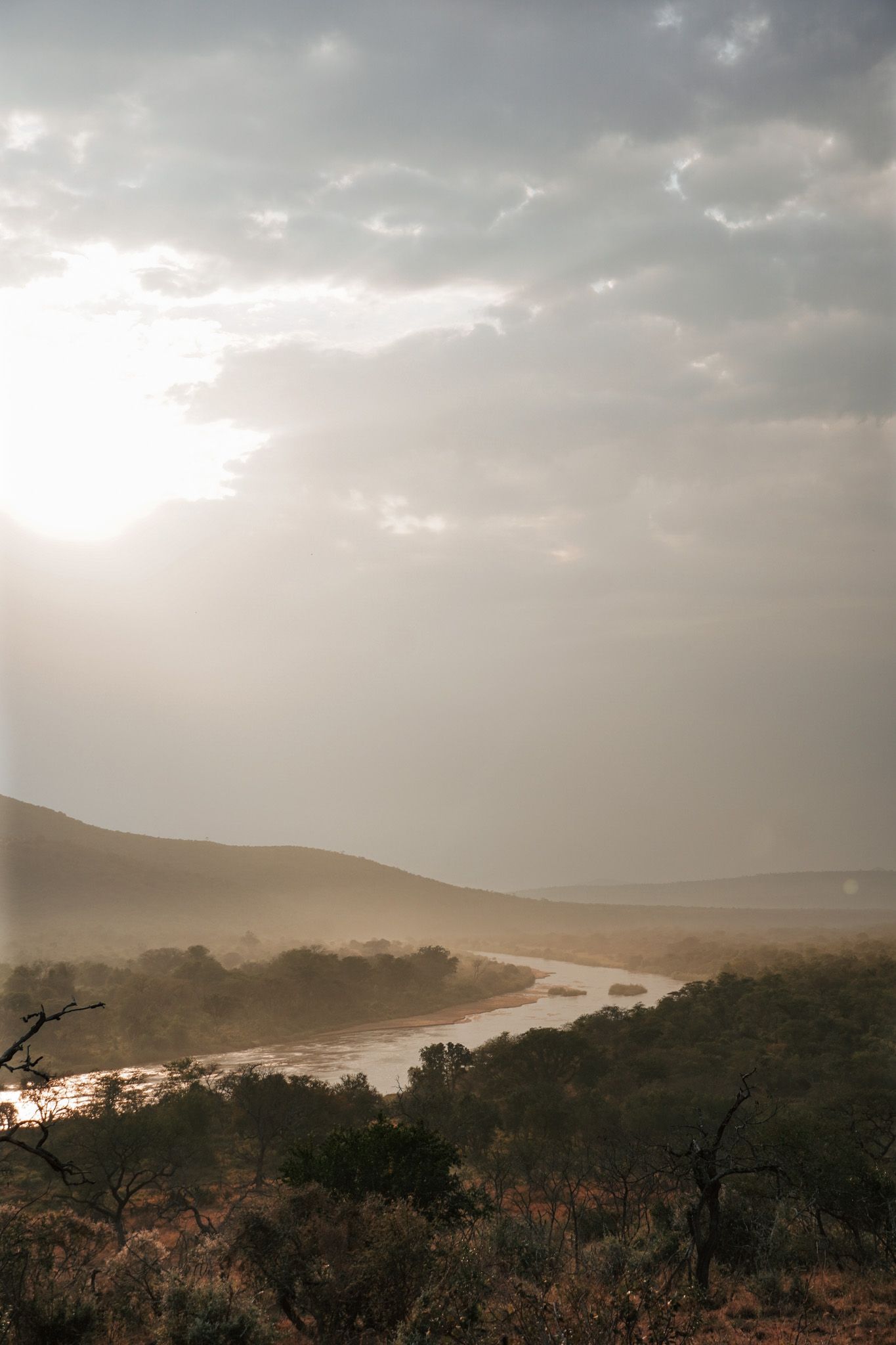 Misty river landscape at sunset with dramatic clouds and rolling hills in the distance.