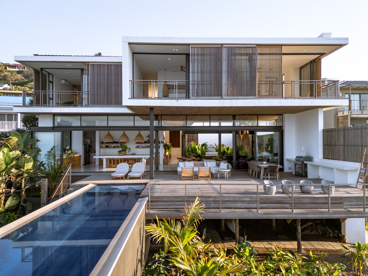 Modern two-story beach house with lap pool and wooden deck surrounded by tropical landscaping.