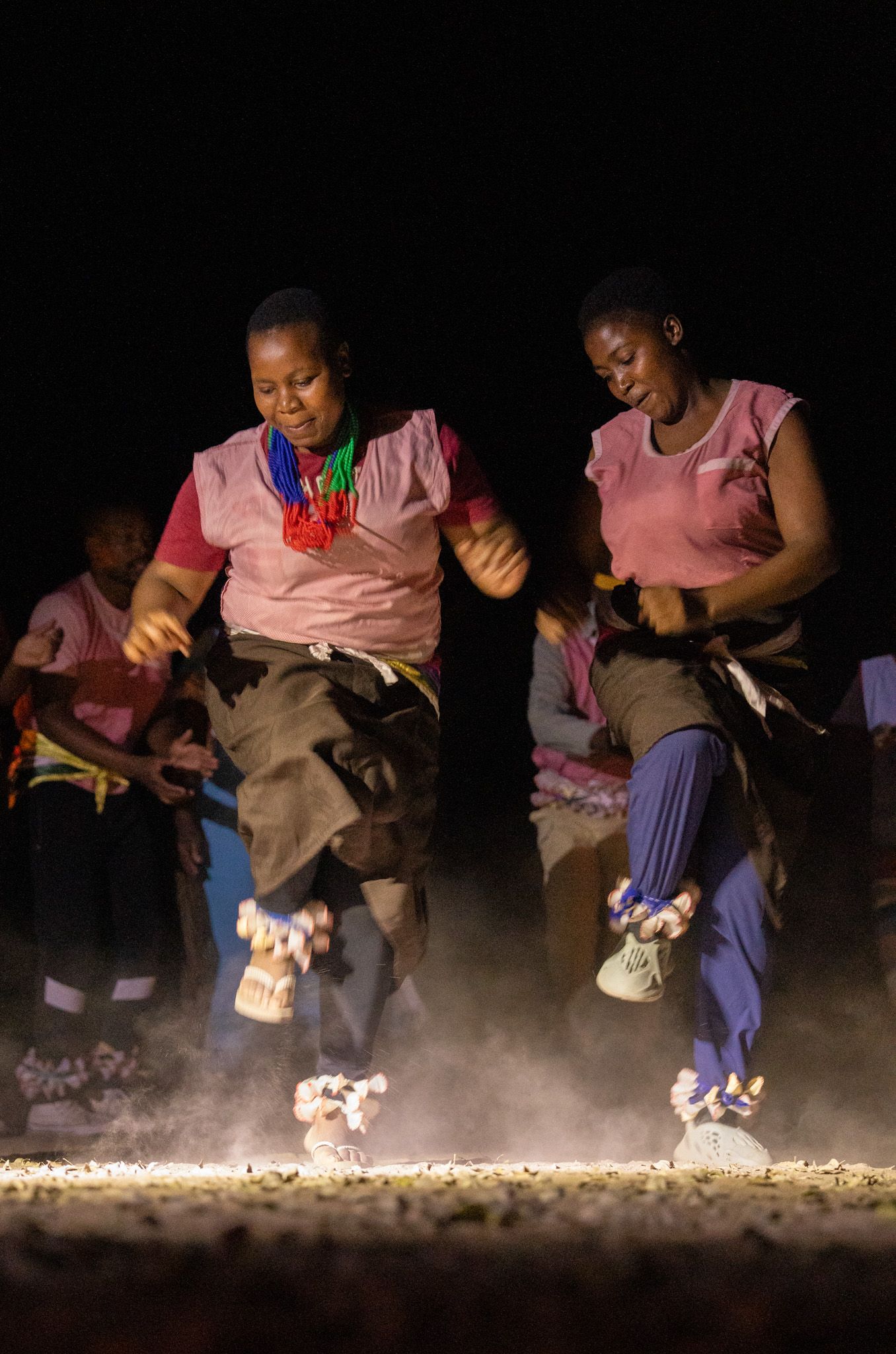 Traditional dancers performing energetic moves with dust rising from their feet in low light.