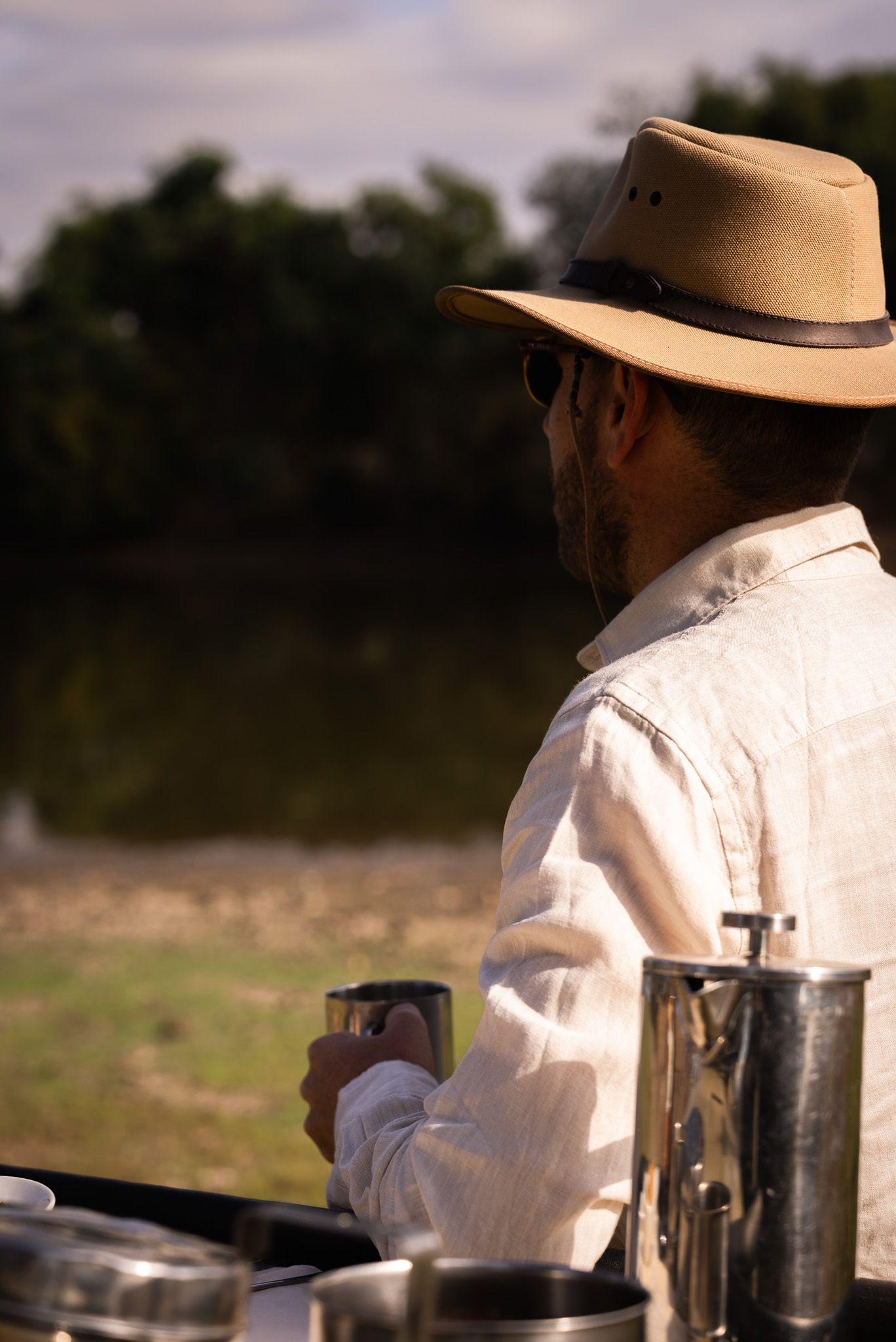 Chef in white coat and hat concentrates while preparing dishes at outdoor kitchen counter.