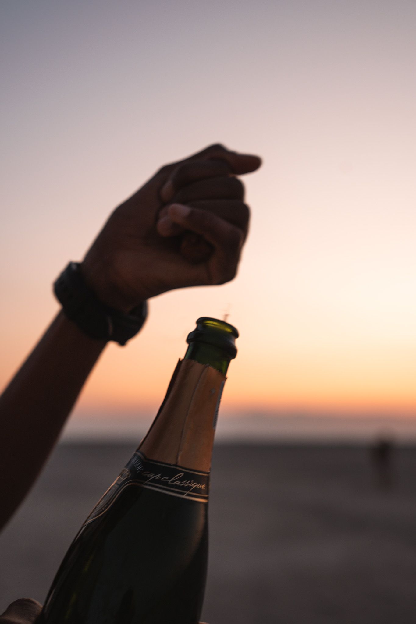 Silhouette of hands opening a champagne bottle at sunset.