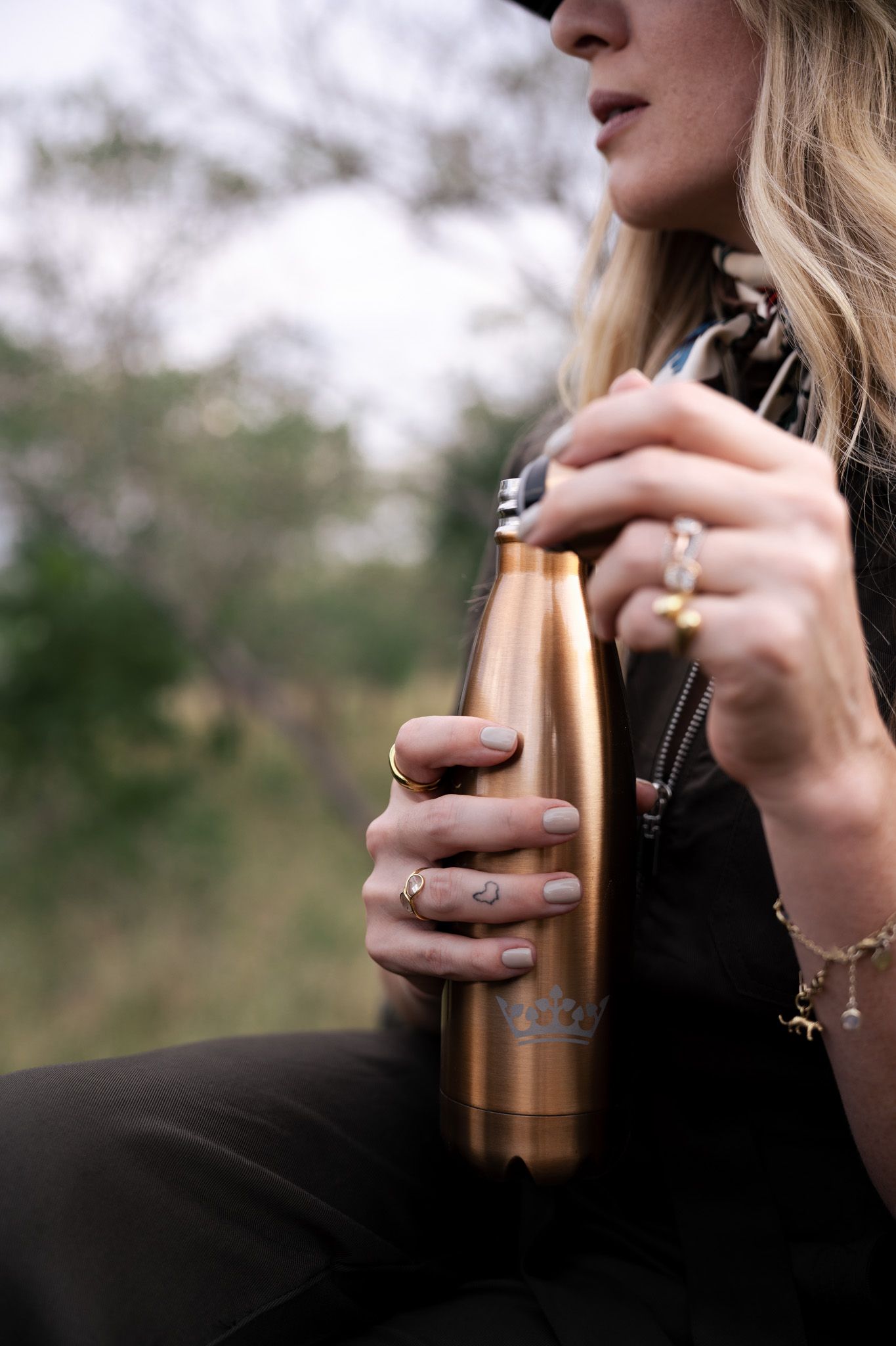 Close-up of hands holding a copper-colored drink container with jewelry details.