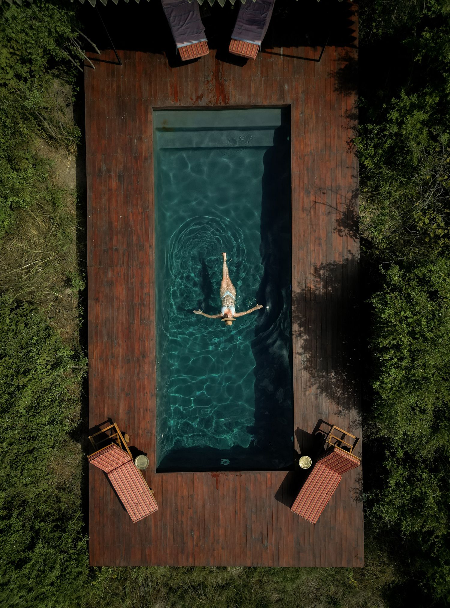 Overhead view of a swimming pool with wooden deck and lounge chairs surrounded by greenery.