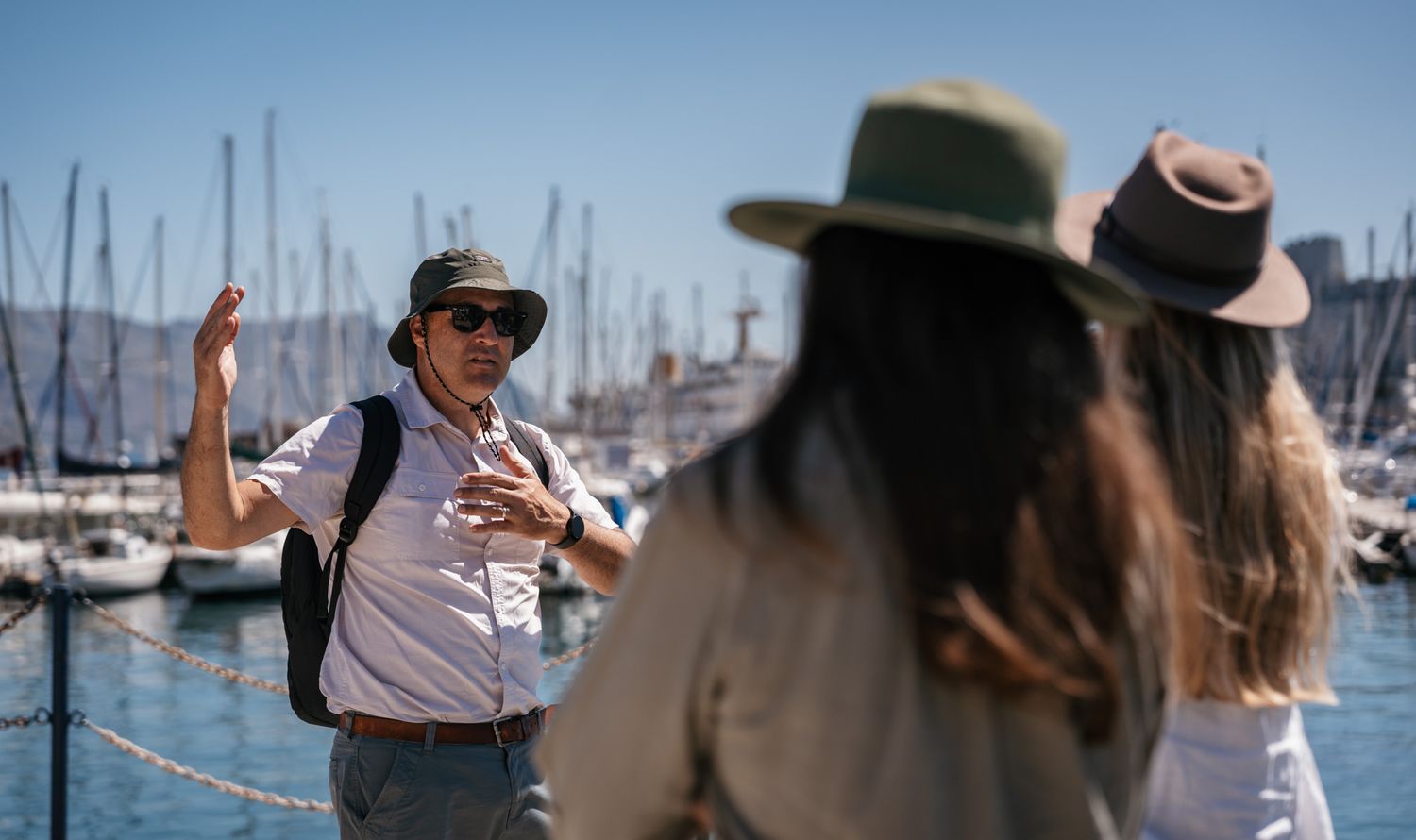 People enjoying a conversation at a marina filled with sailboat masts.
