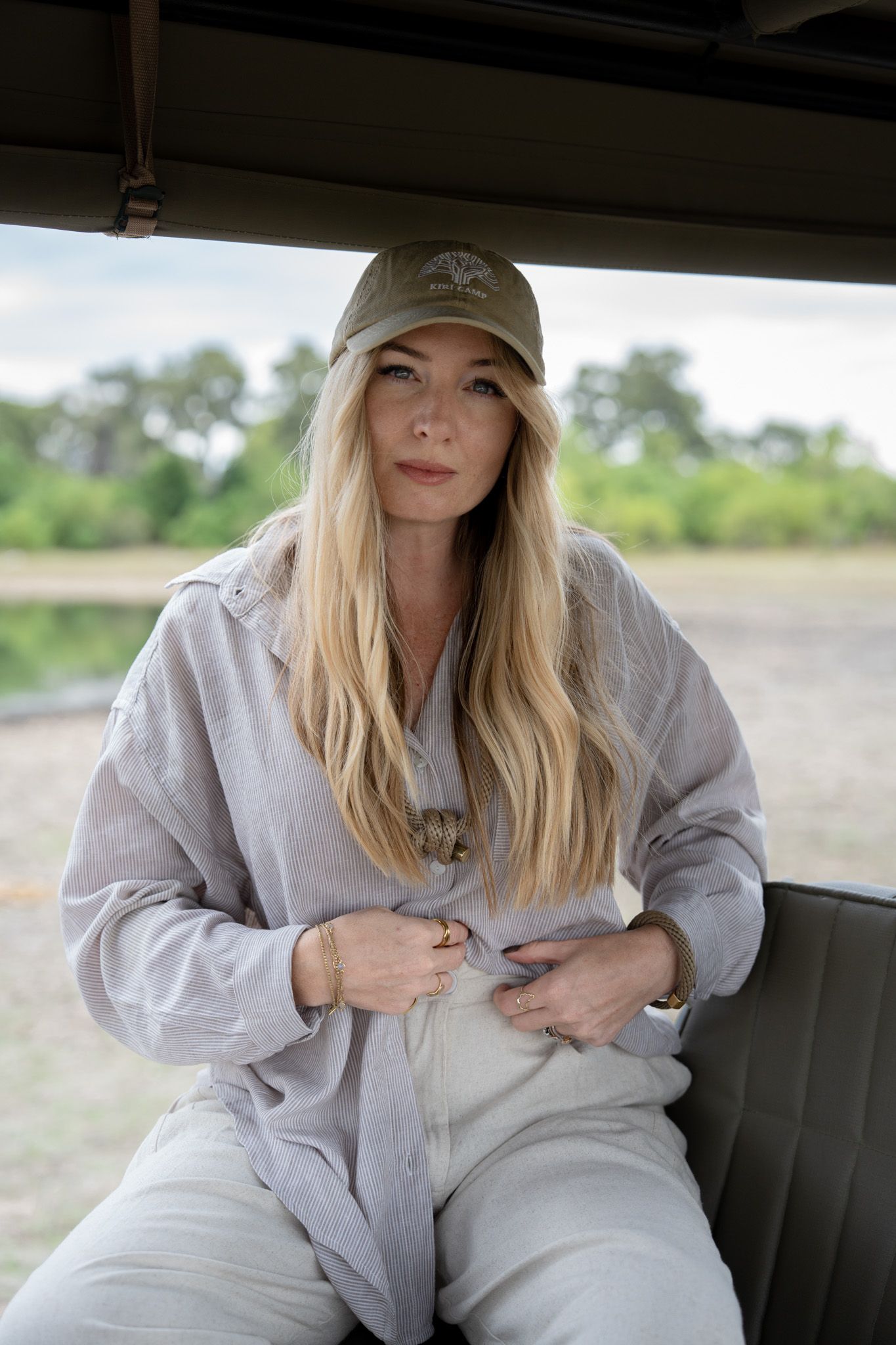 Someone wearing a gray baseball cap and linen jumpsuit sits in what appears to be the back seat of a vehicle.
