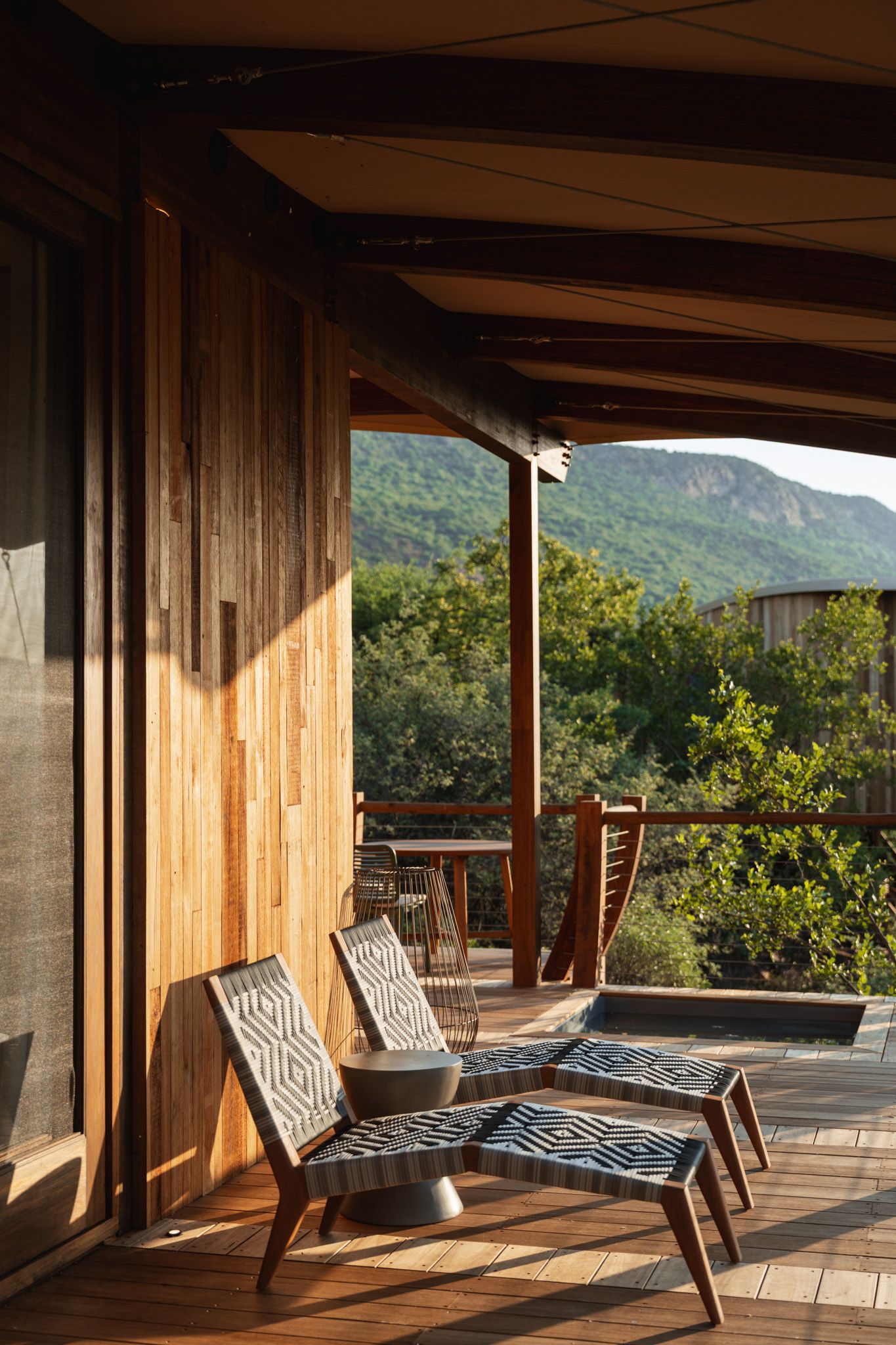 Modern deck with striped lounge chairs overlooking mountain views in golden sunlight.