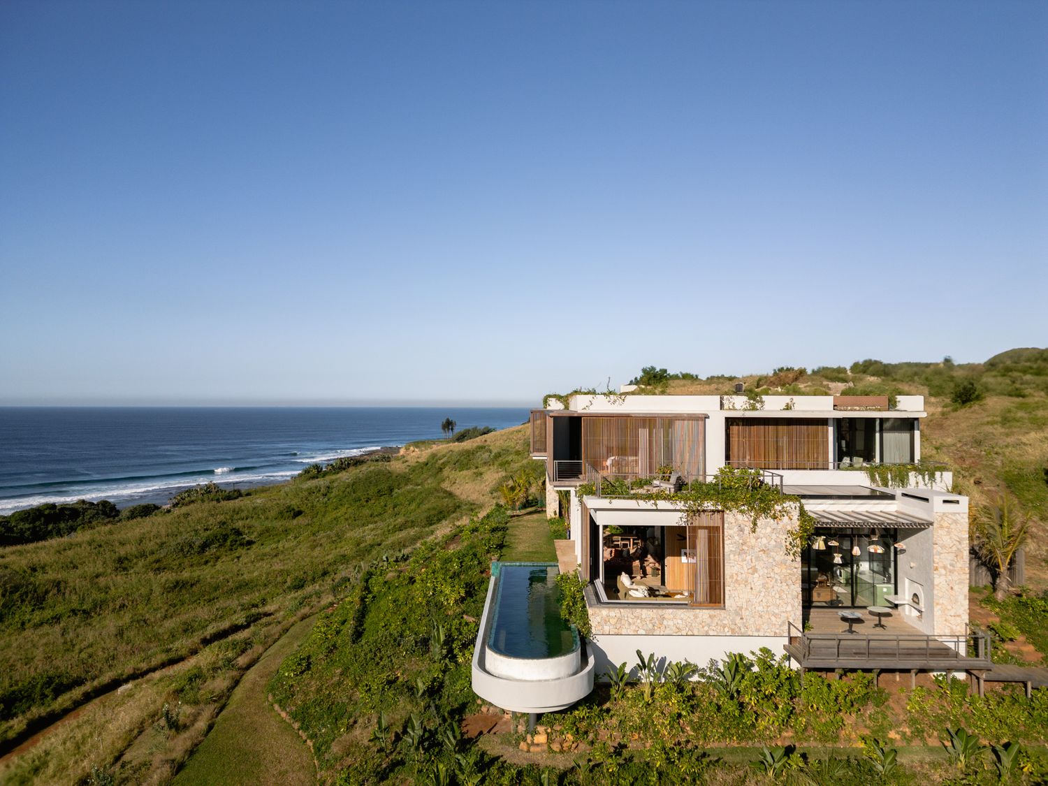 Modern luxury villa with infinity pool perched on coastal cliffs overlooking the ocean.