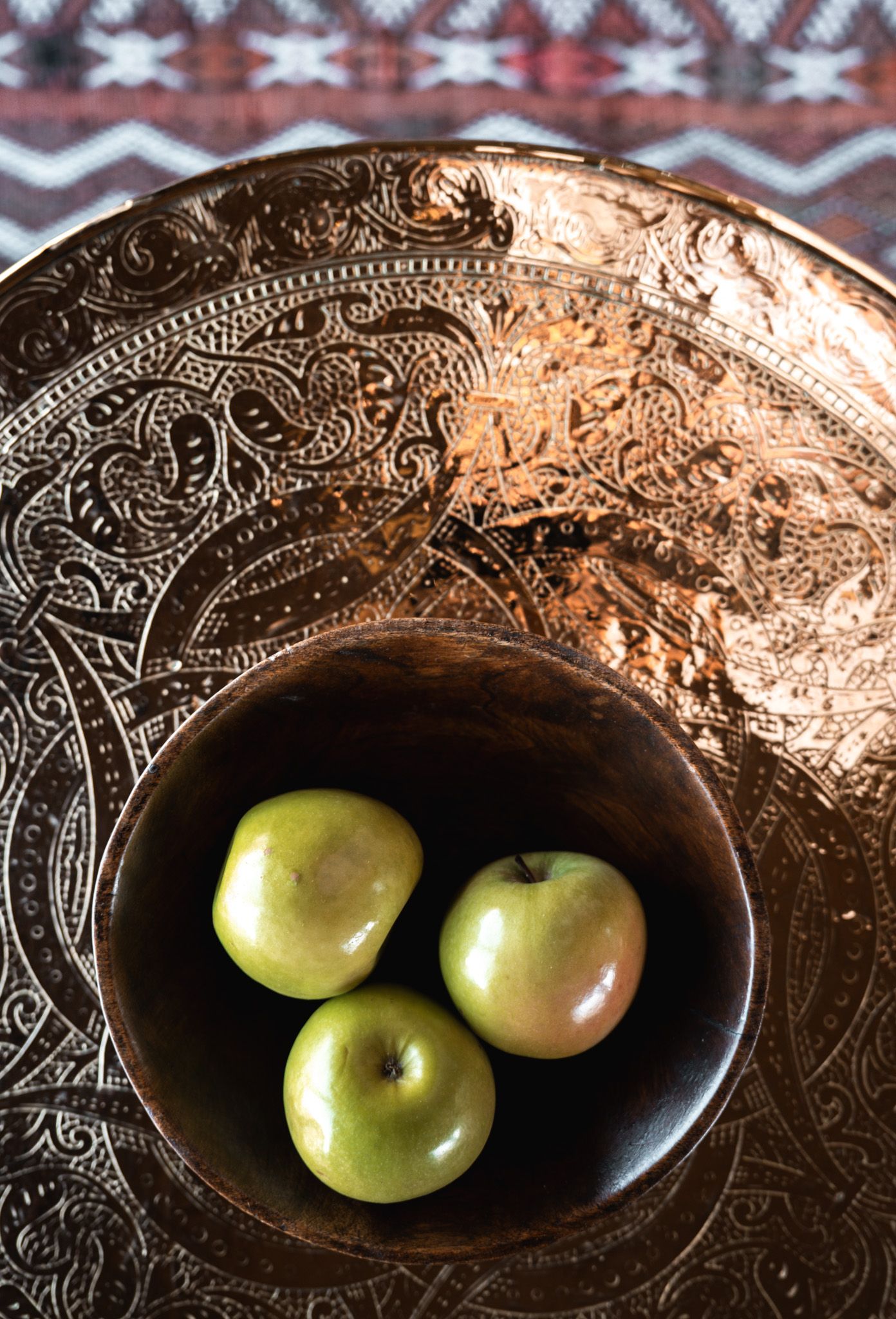 Three green apples in a decorative metal bowl with intricate paisley patterns.