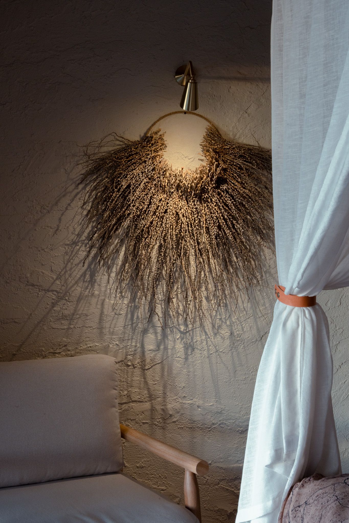 Artistic dried grass wall sconce creating dramatic shadows against white wall.