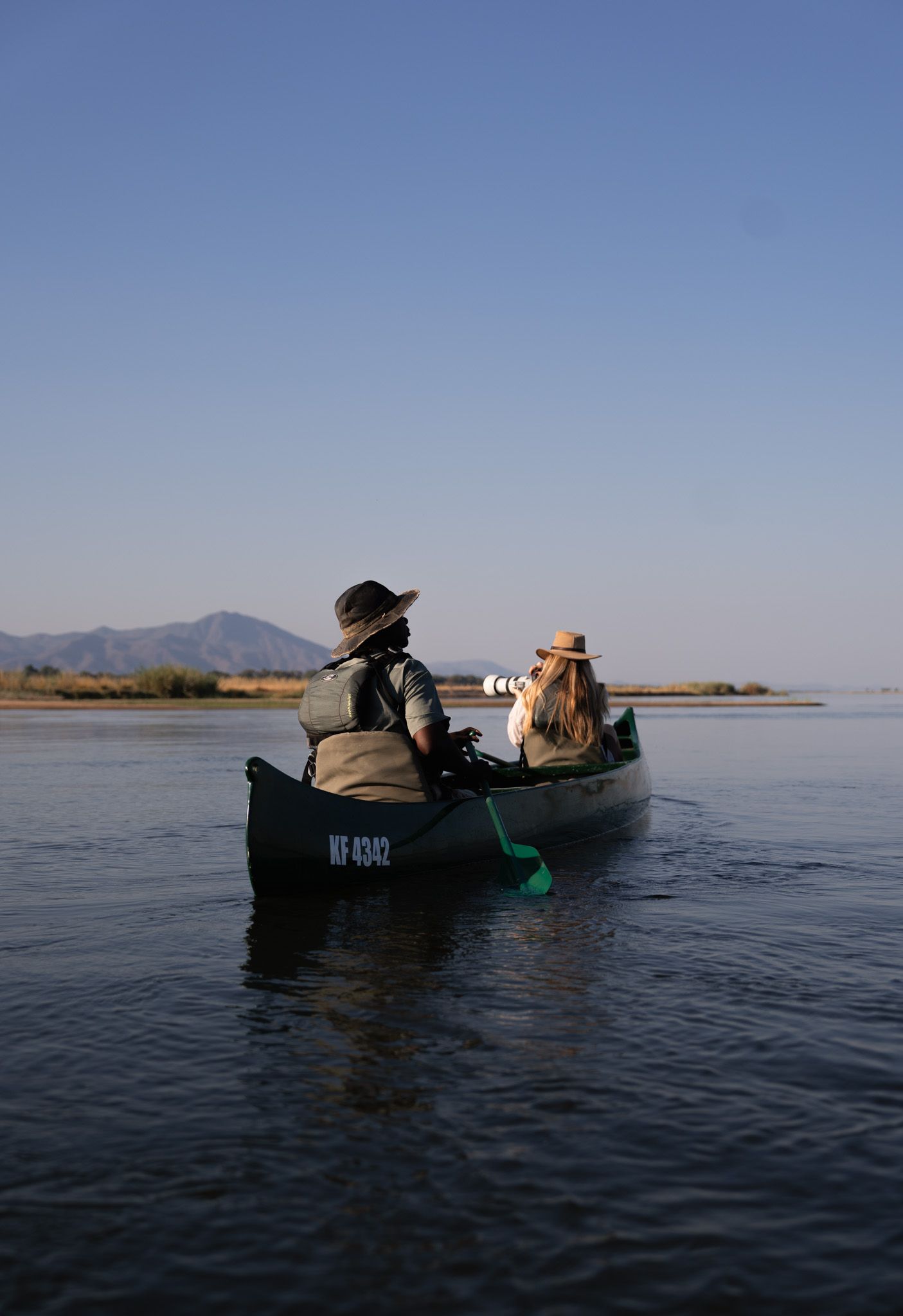 Canoes gliding across calm waters with mountains in the background.