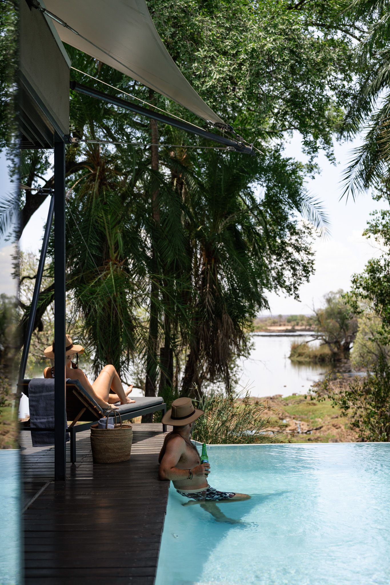 Infinity pool overlooking nature with wooden deck and palm trees.