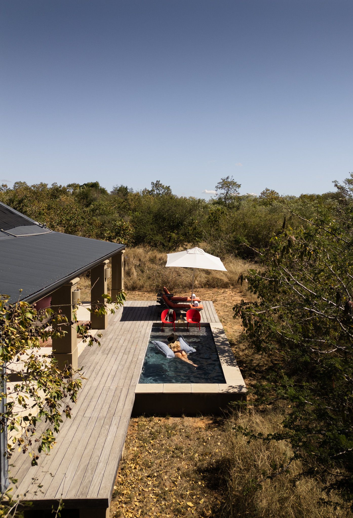 Modern poolside deck with red furniture surrounded by natural landscape.