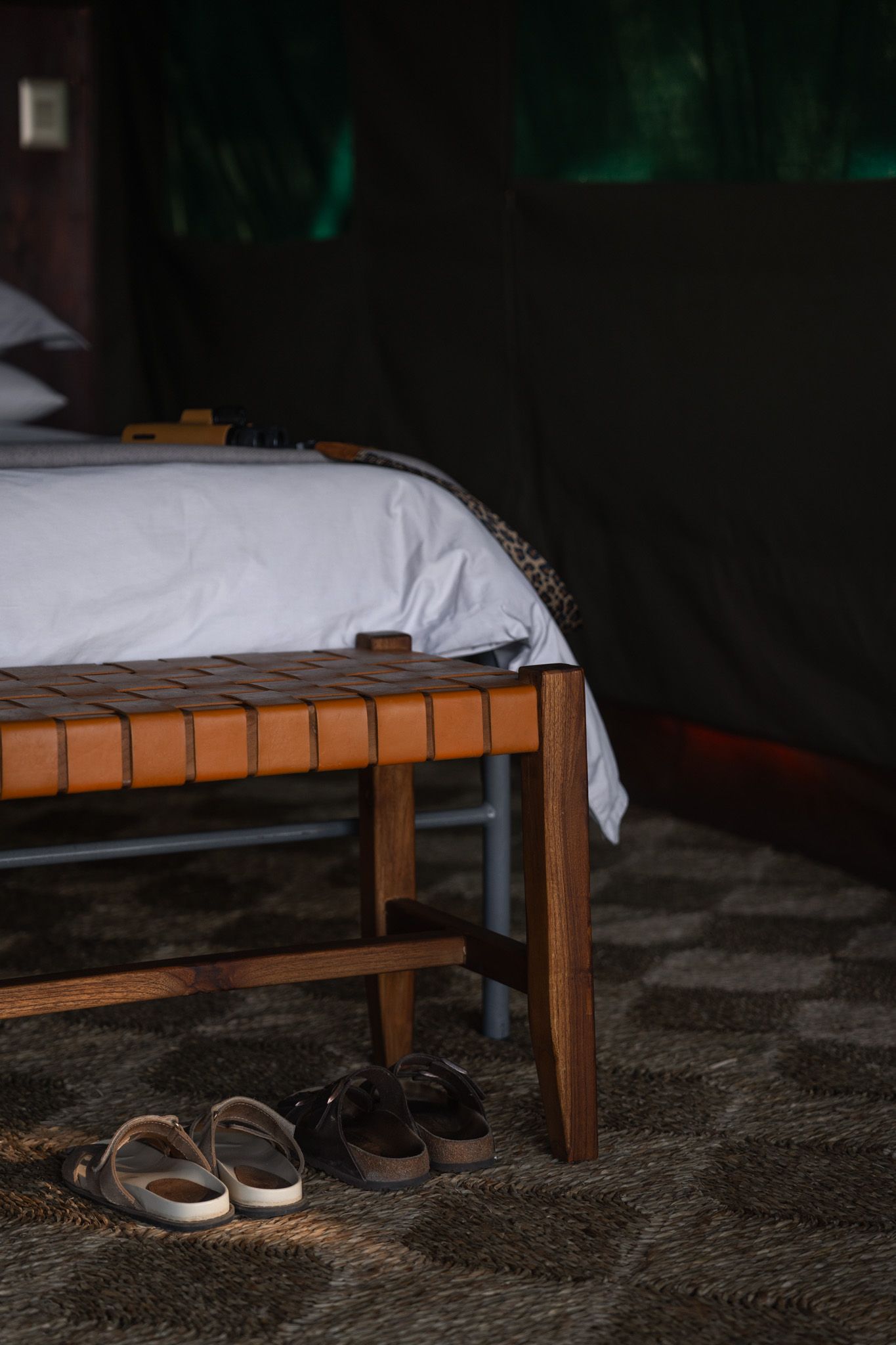 Minimalist bedroom corner with wooden bed frame and casual shoes on dark flooring.