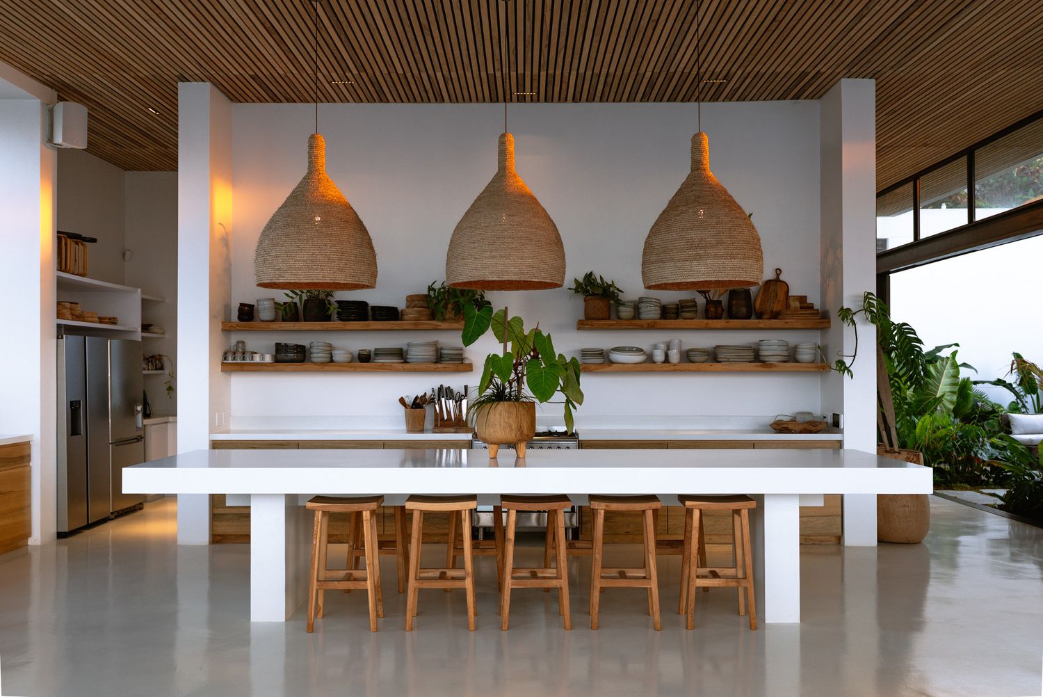 Minimalist dining area featuring large white island and three woven pendant lights above.
