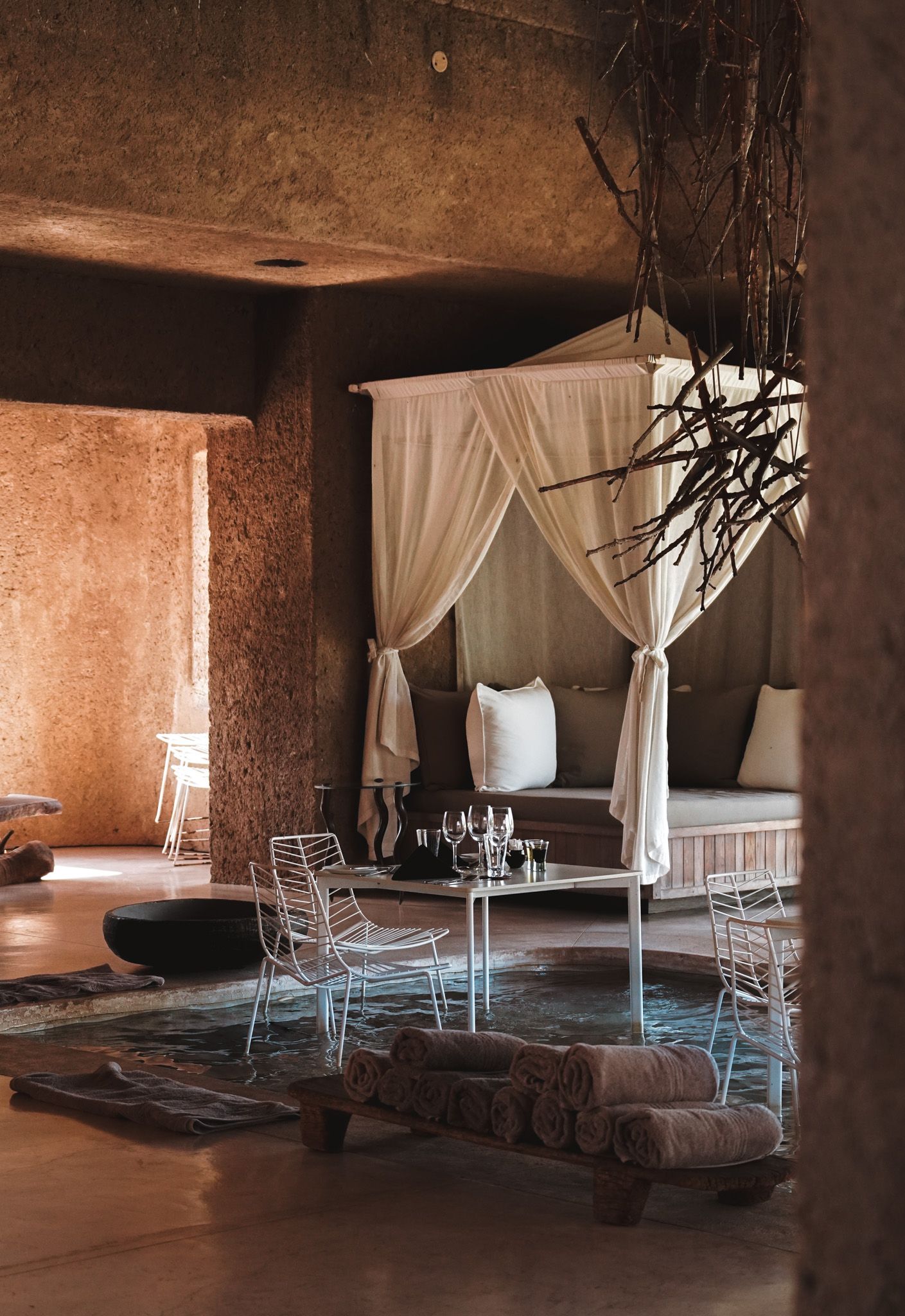 Rustic safari lodge interior with draped white canopy beds and stone walls creating an atmospheric sleeping space.