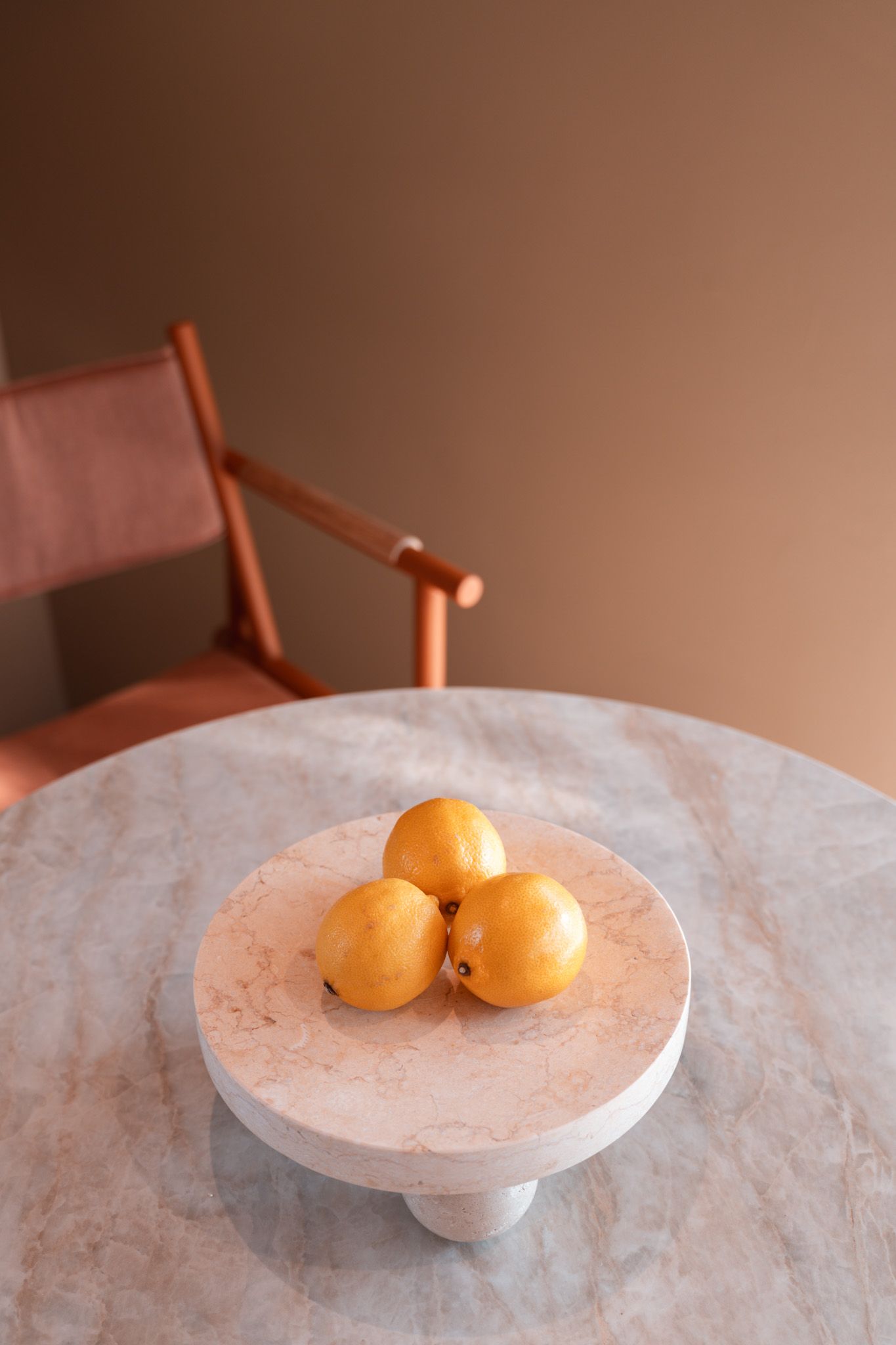 Fresh oranges displayed on a round marble pedestal against a warm neutral background.
