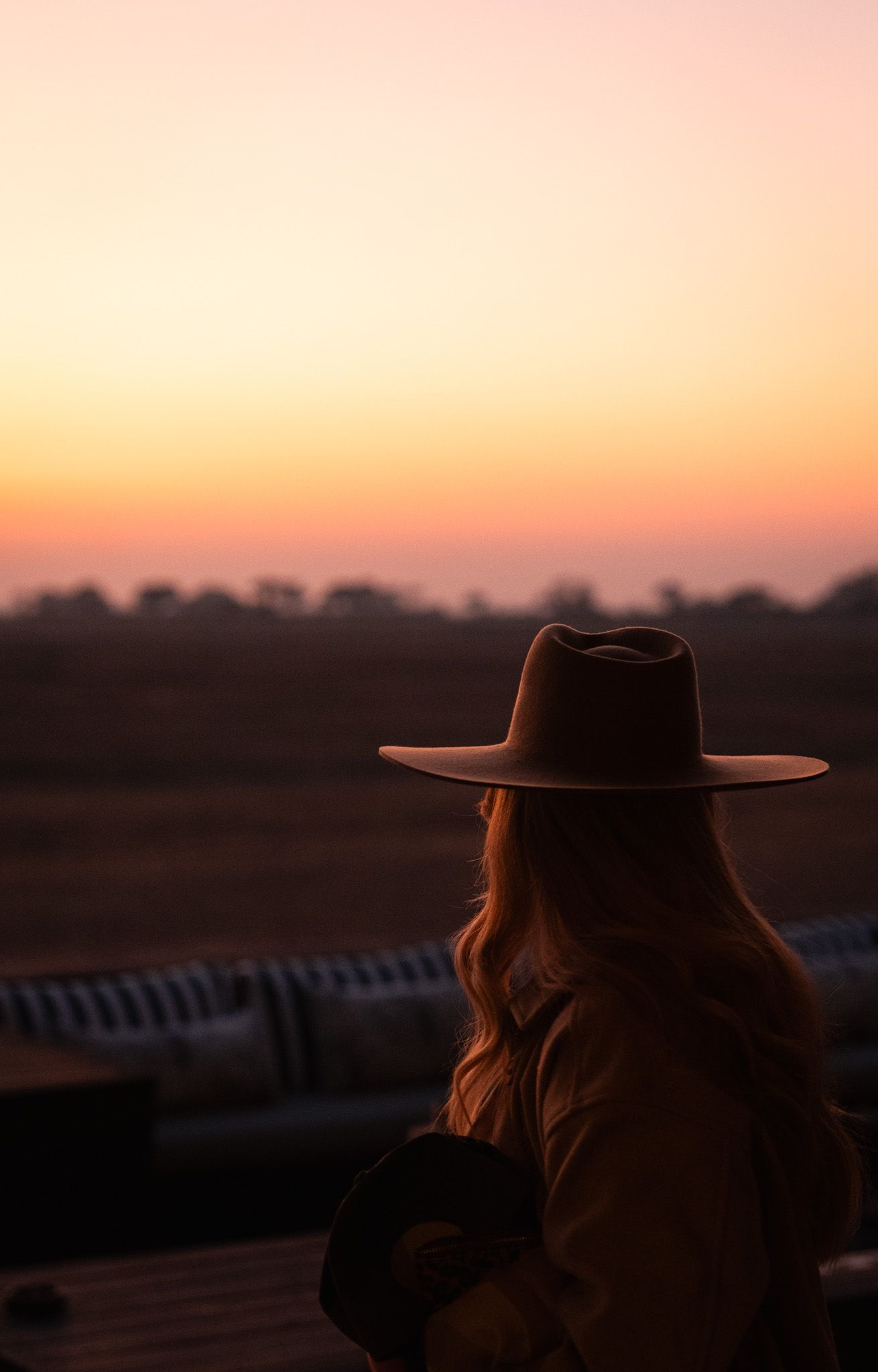 A silhouette against a vibrant sunset sky shows a person wearing a wide-brimmed hat at dusk.