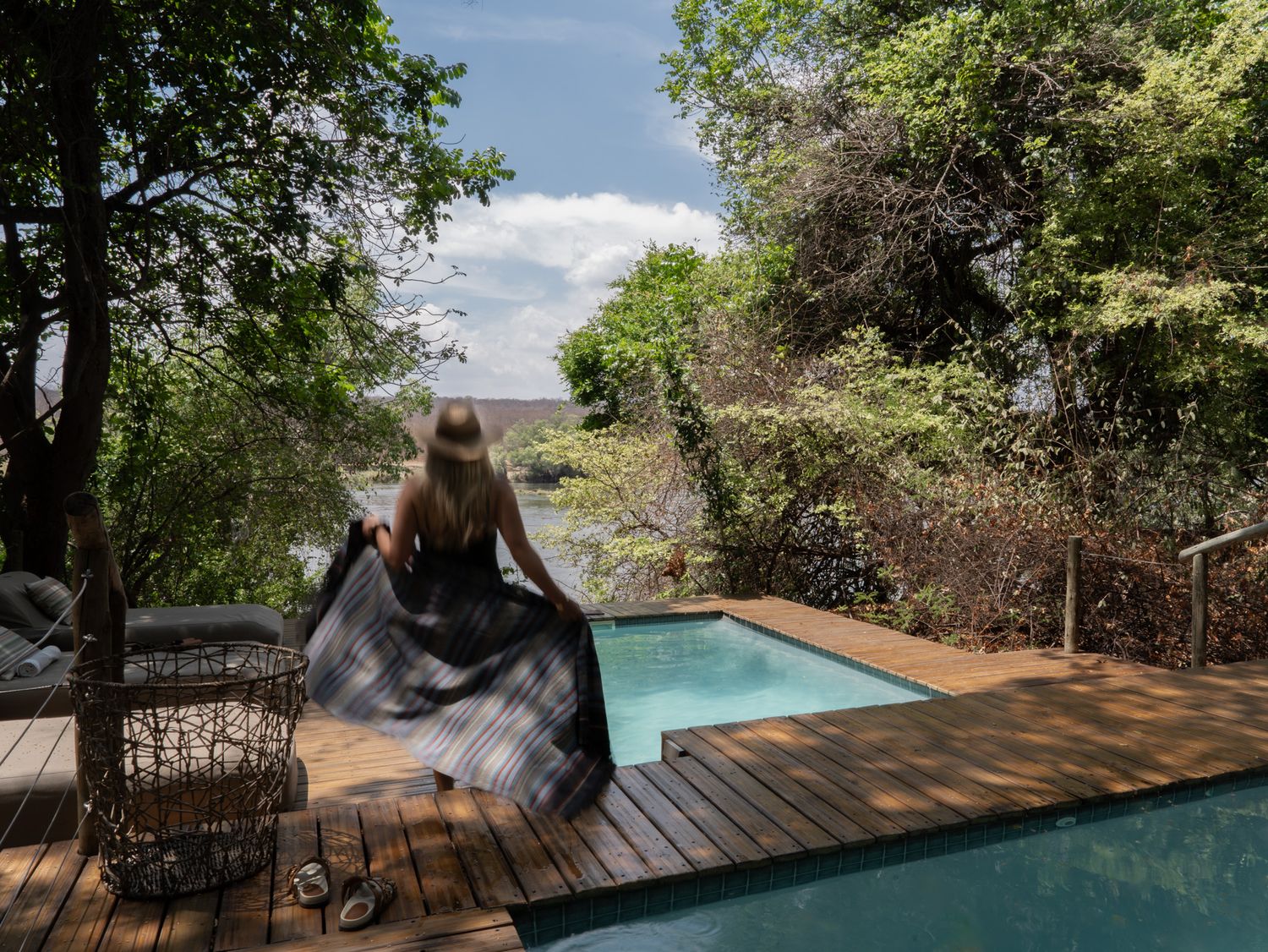 Wooden deck with infinity pool overlooking natural landscape on sunny day.