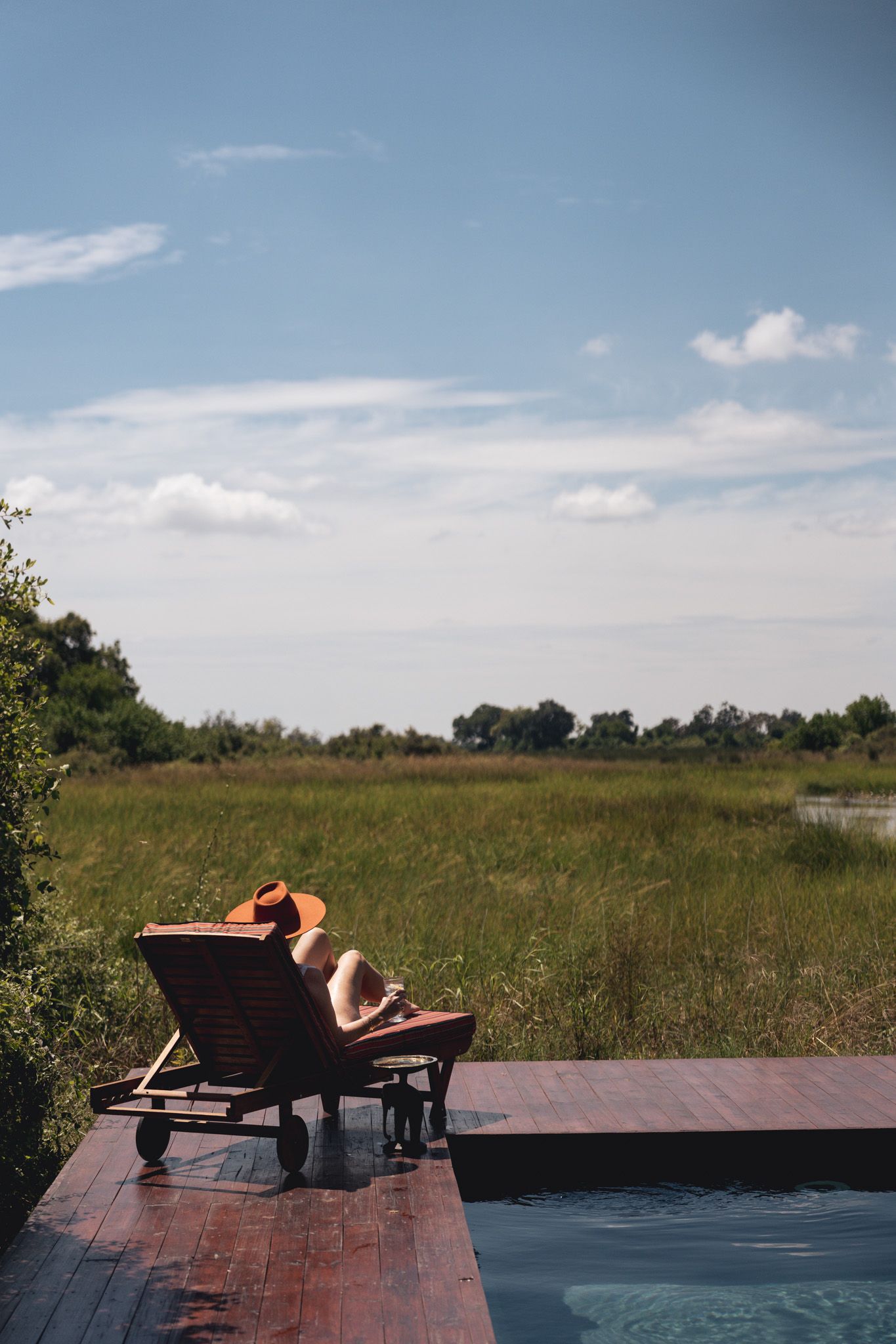 Lounger chair overlooking a swimming pool and natural grassland landscape.